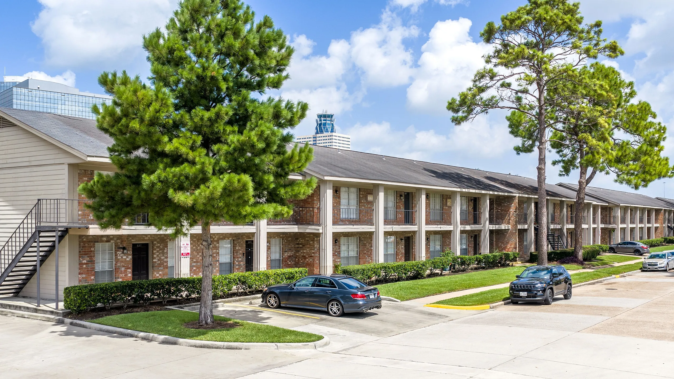 Charming two-story apartment complex with ample parking, lush green landscaping, and a serene suburban ambiance.