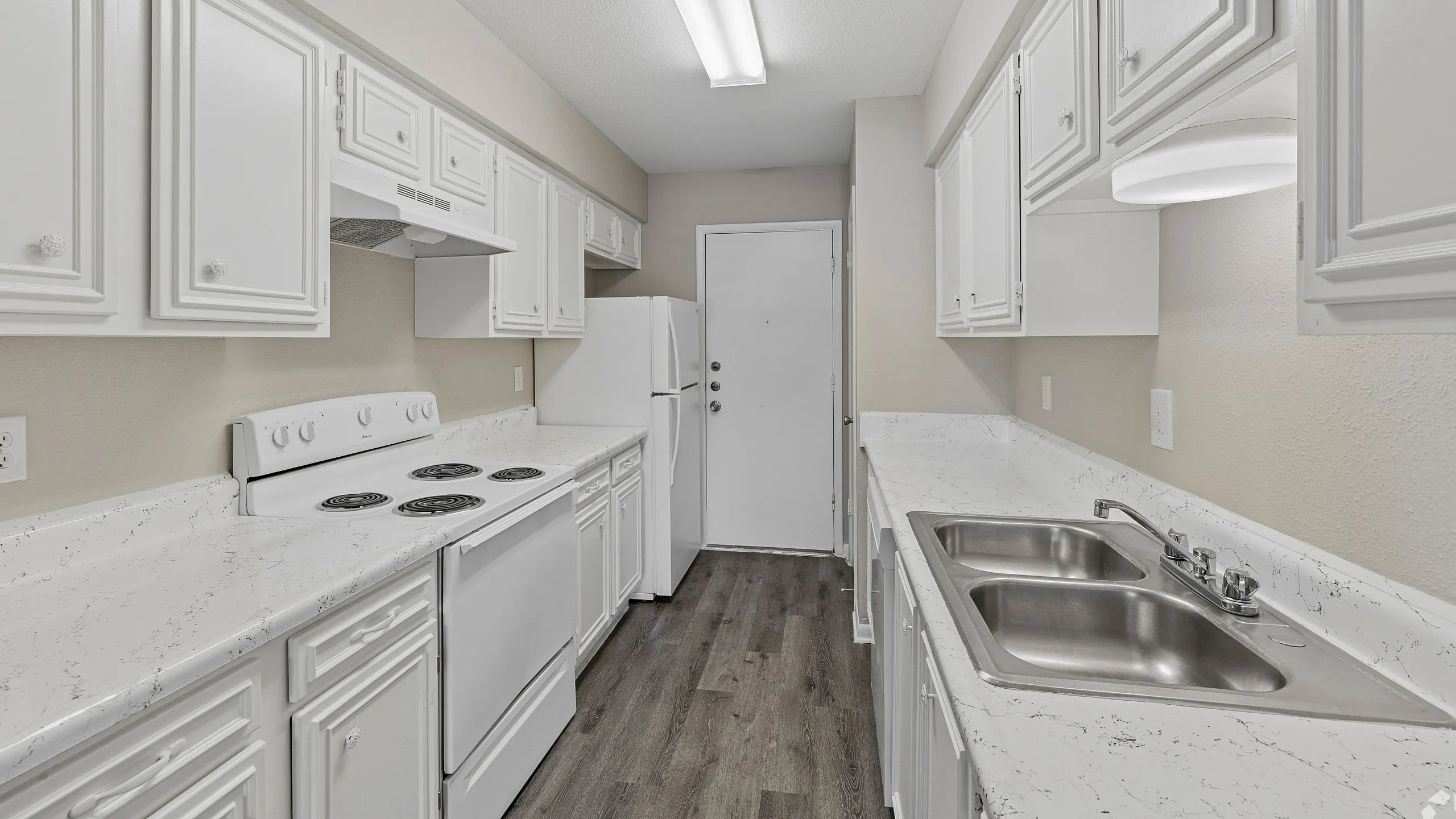 Elegant galley kitchen with pristine white cabinetry, modern appliances, and sleek marble-style countertops.