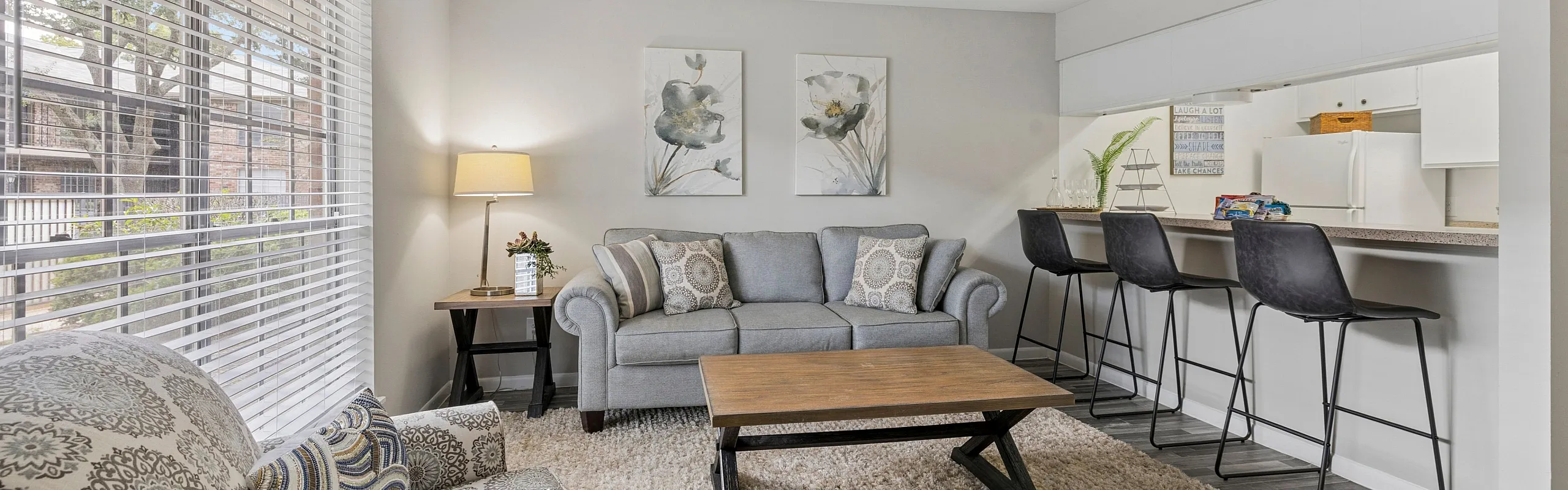 Bright and airy living room with stylish decor, featuring cozy seating, modern art, and a breakfast bar adjoining the kitchen.