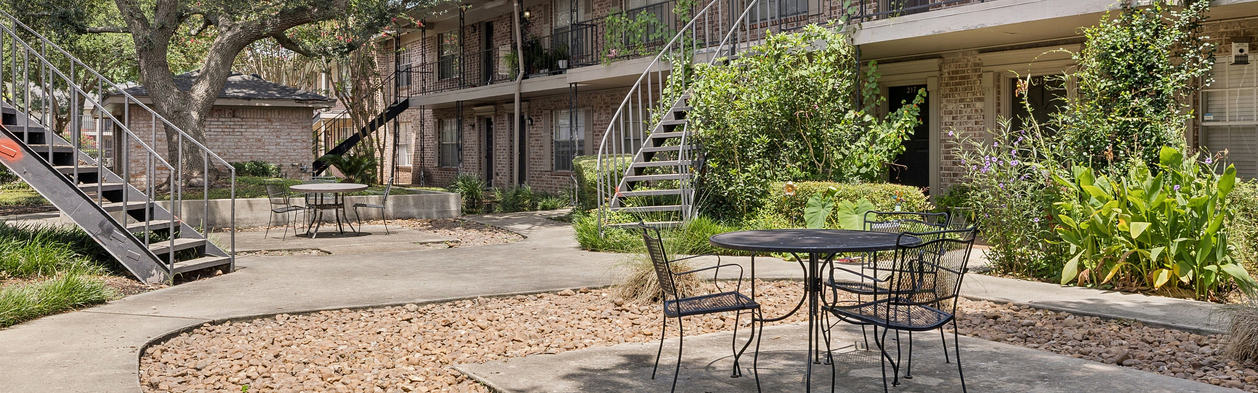 Charming courtyard with lush greenery and inviting seating area in a serene apartment complex setting.