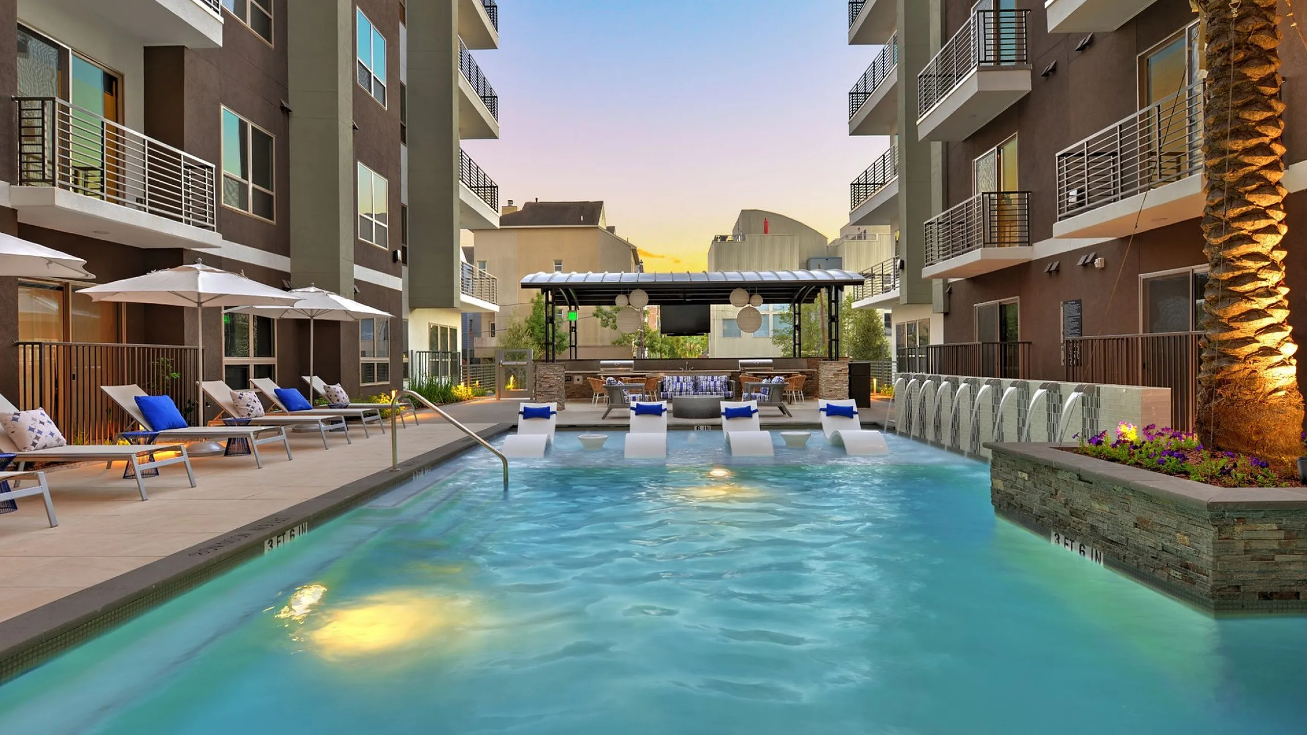 Pool courtyard with lounge chairs, umbrellas and mid-rise buildings at sunset, Houston, TX