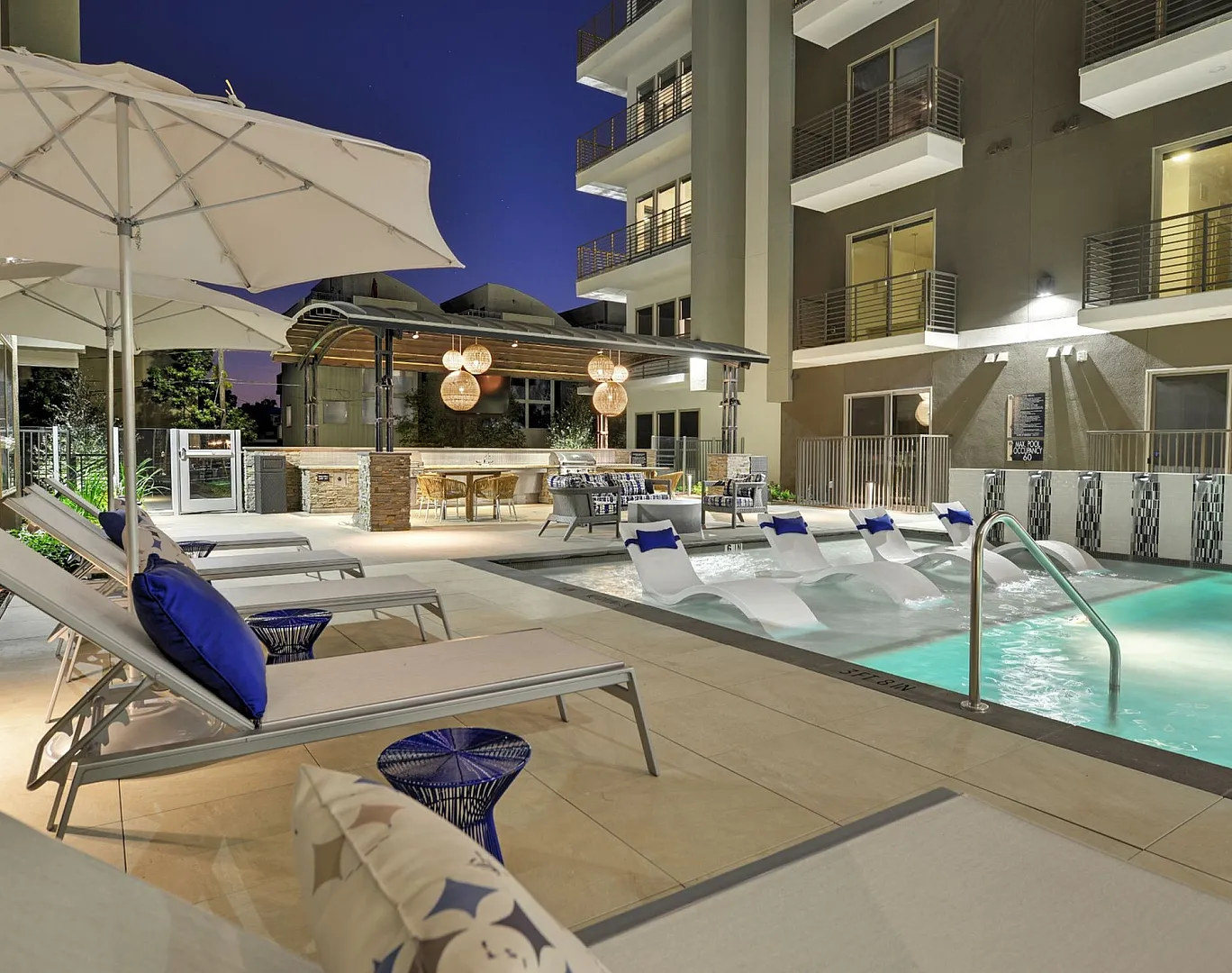 Pool with lounge chairs, umbrellas and mid-rise building at dusk, Houston, TX