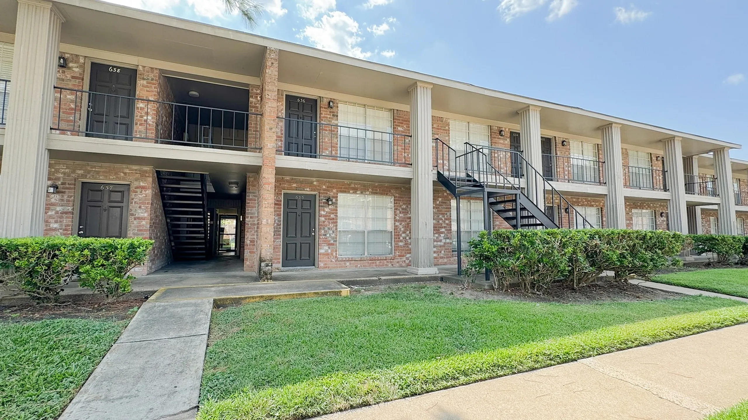 Two-story brick building with balconies, exterior stairs, hedges and lawn, Memorial City, Houston TX