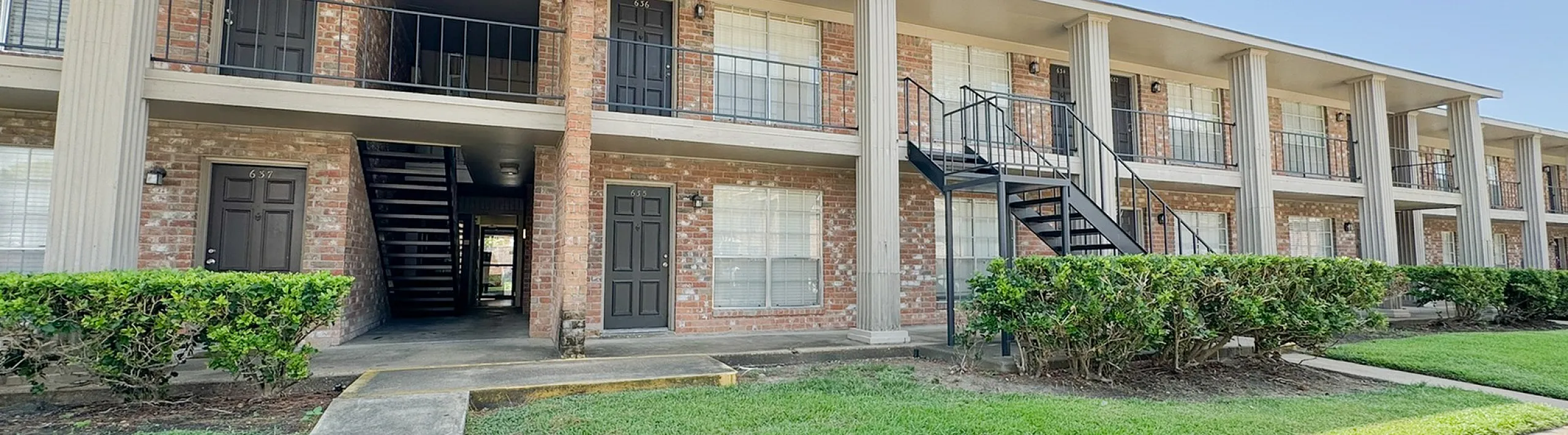 Two-story brick building with balconies, exterior stairs, hedges and lawn, Memorial City, Houston TX