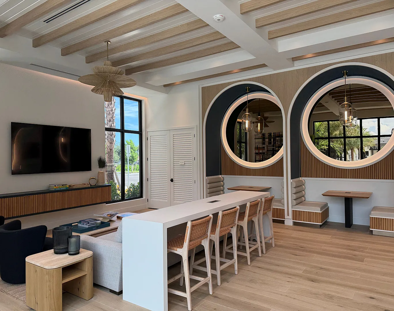 Pool pavilion lounge with wood beam ceiling, round windows, bar seating, and wall-mounted TV