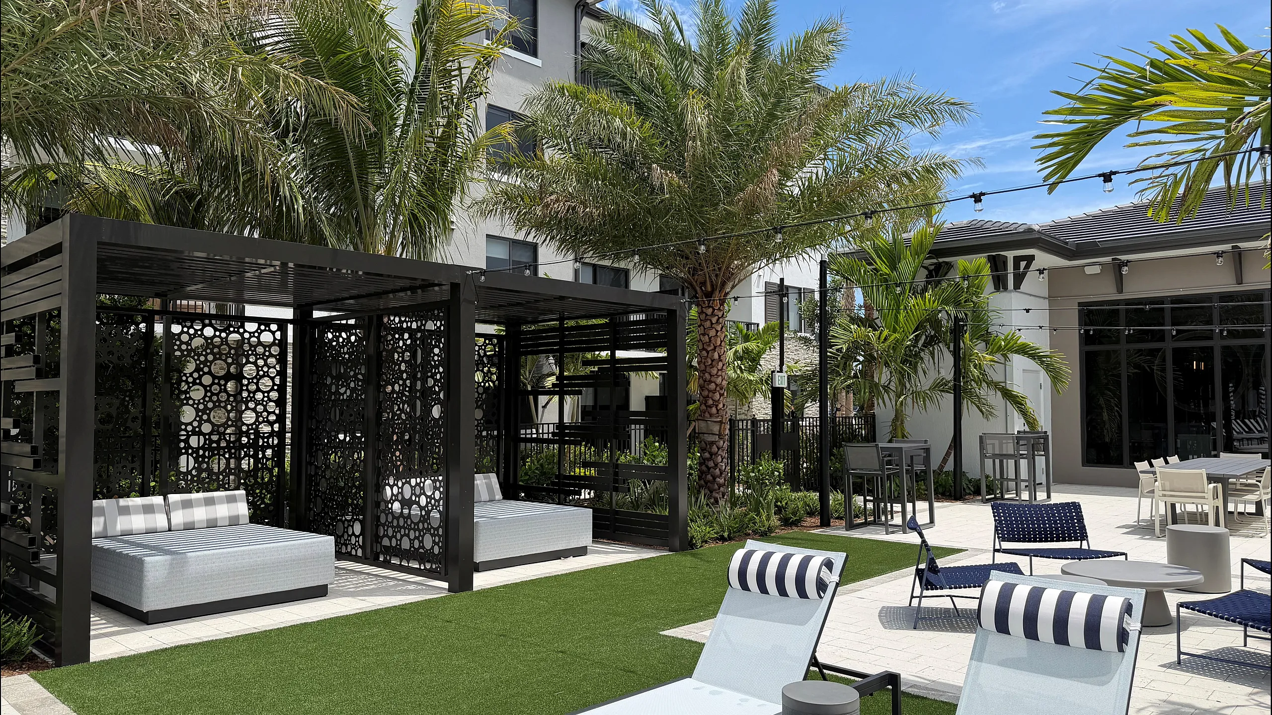Pool deck with lounge chairs, cabana daybeds, string lights, and palm trees in Pompano Beach