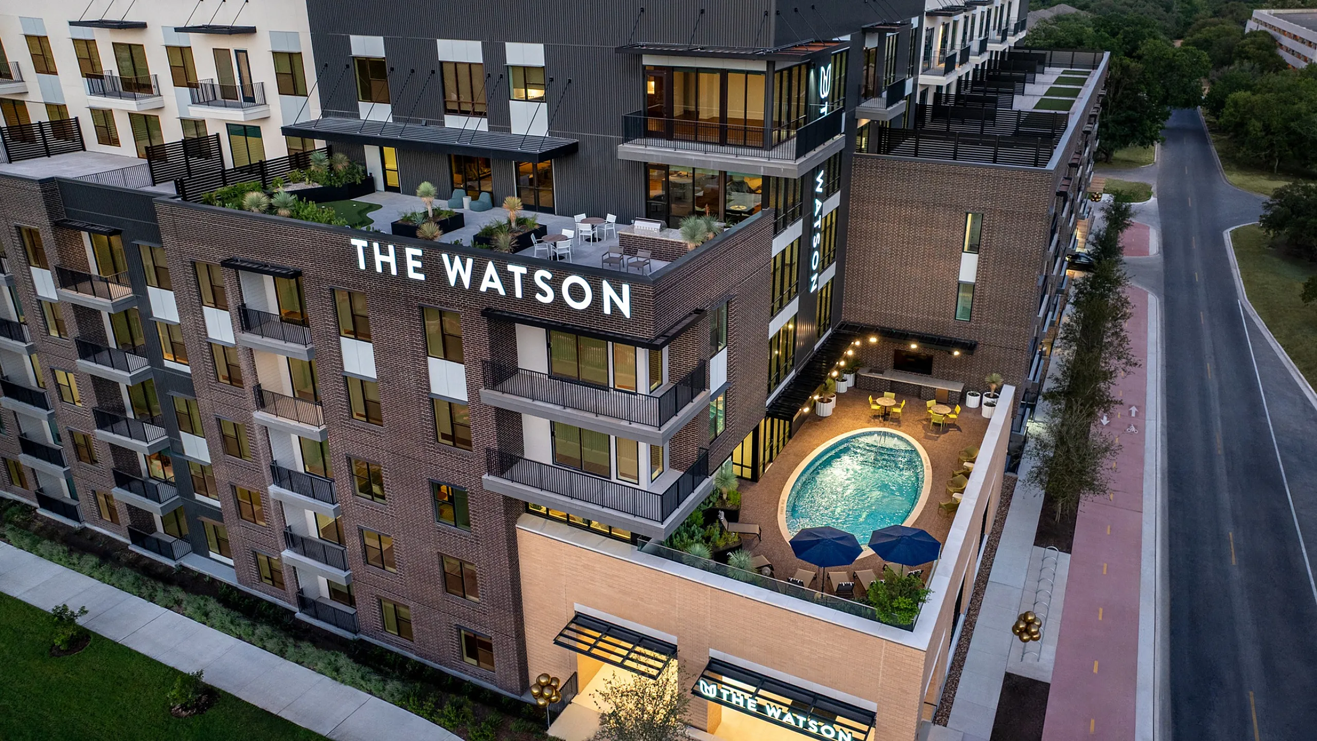 Aerial view of apartment building in Austin with rooftop terrace, building signage and courtyard pool with umbrellas