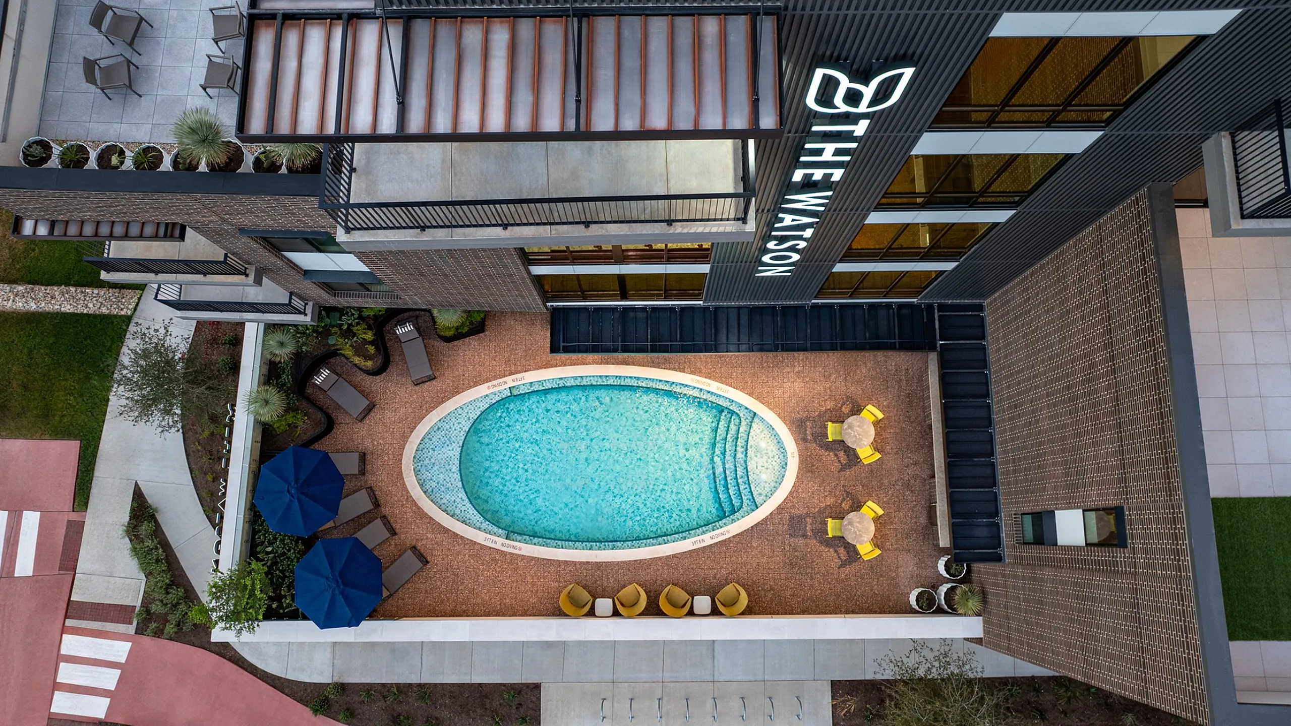 Aerial view of courtyard pool in Austin with lounge chairs, blue umbrellas and yellow patio seating