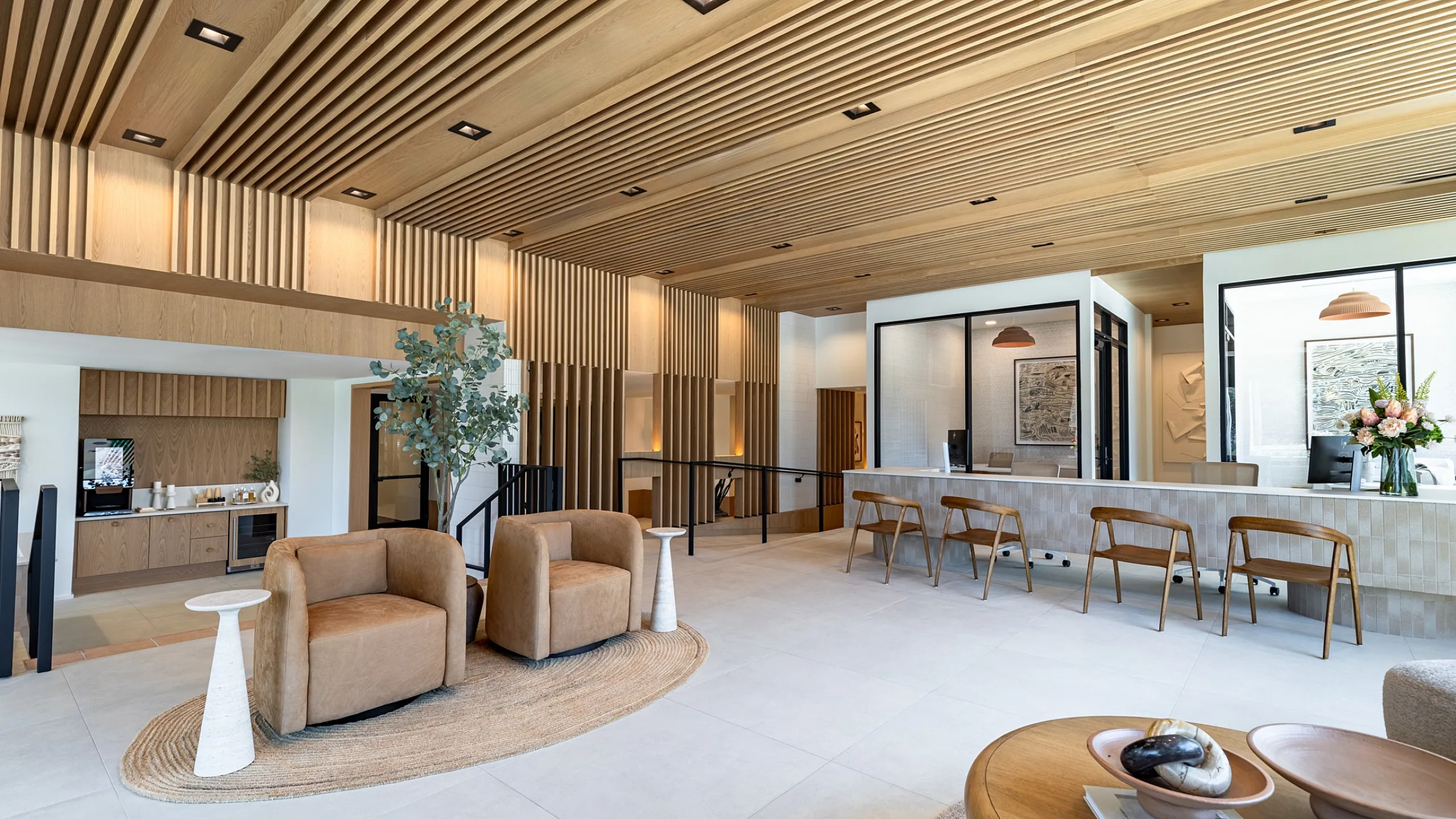 Lobby with wood slat ceiling, two lounge chairs, coffee bar and a counter with wood chairs