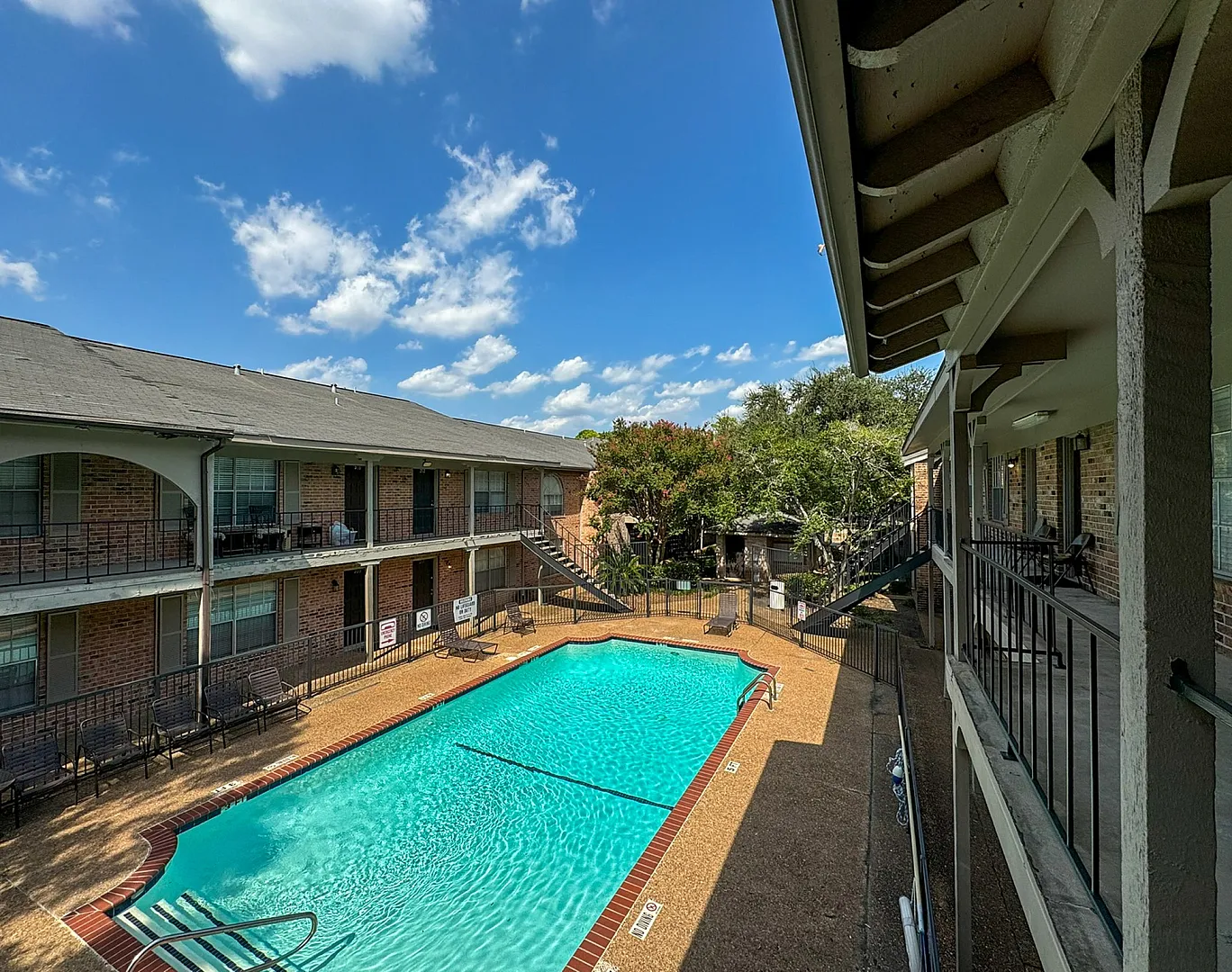 Courtyard pool seen from upper walkway with brick deck, iron fence and shade trees, Memorial City, Houston TX