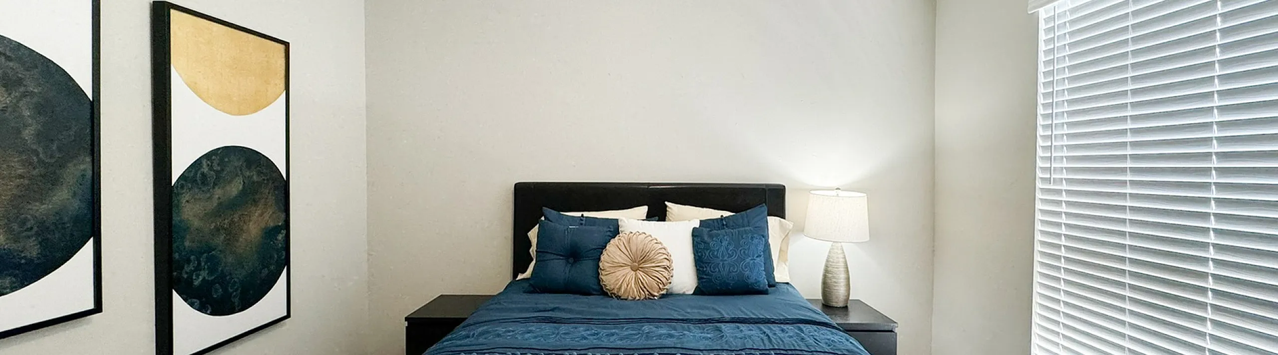 Bedroom with carpet, blue bedding, nightstand lamp, wall art and window blinds
