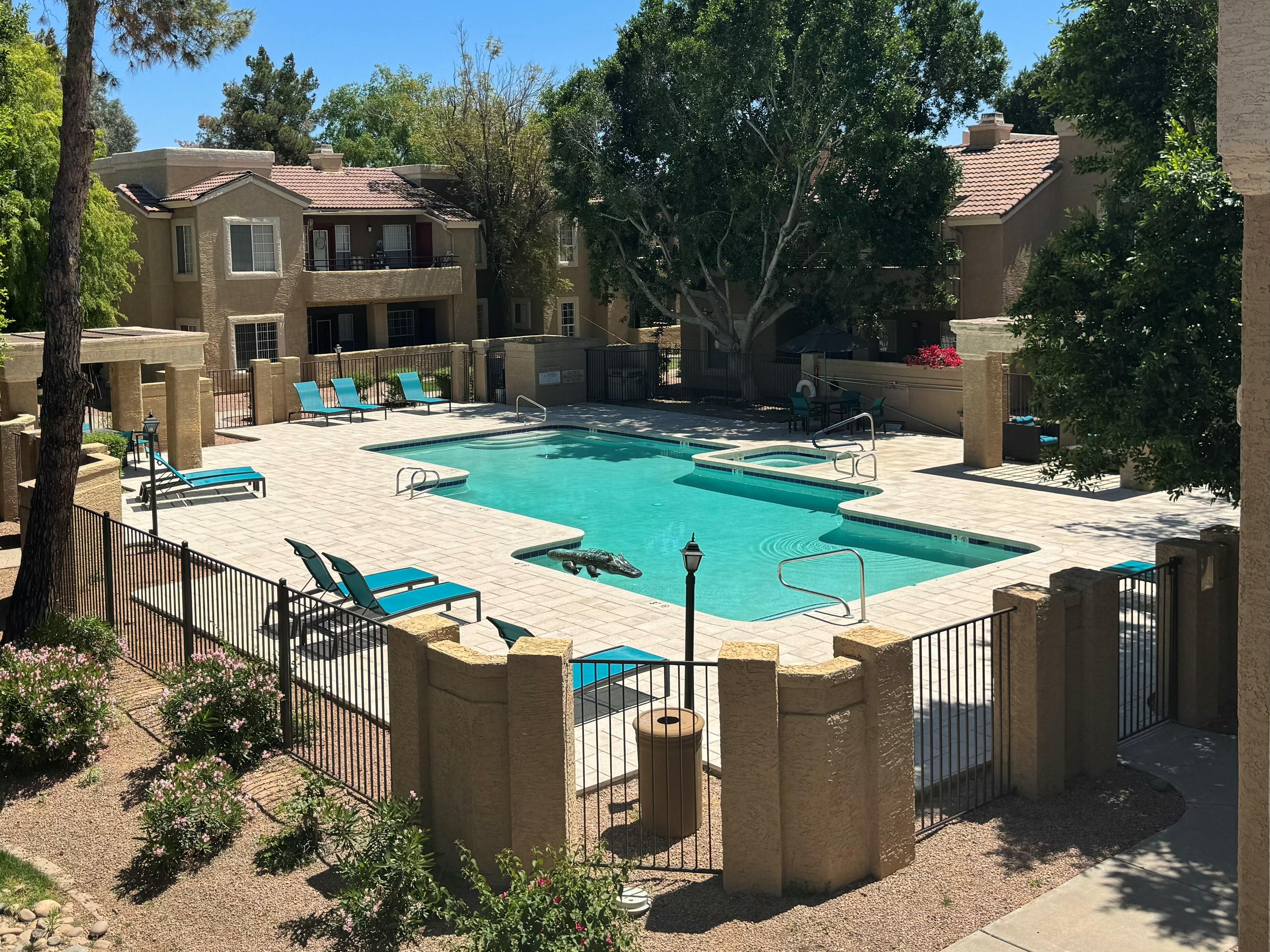 Inviting apartment complex with a sunlit swimming pool, surrounded by lush greenery and comfortable lounge chairs.