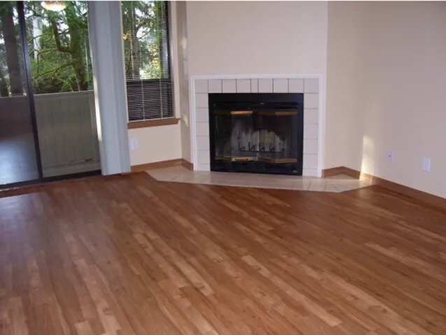 Inviting living room with elegant hardwood floors, a cozy fireplace, and a view of lush greenery through the large glass doors.