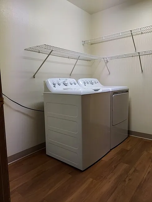 Modern laundry room featuring a sleek washer and dryer set, enhanced by elegant wooden flooring and efficient shelving.