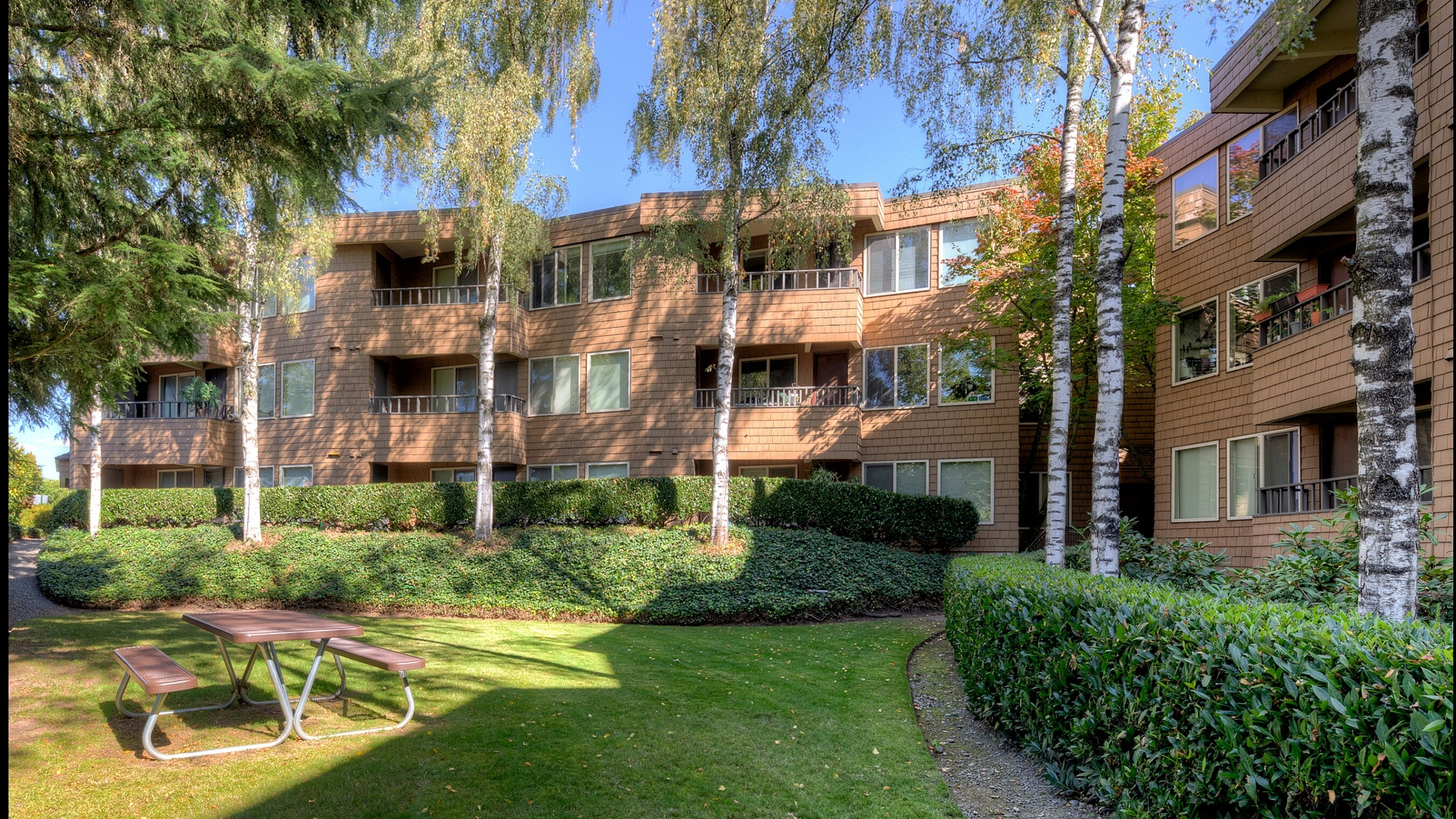 Charming apartment building nestled in lush greenery with inviting balconies and a serene outdoor picnic area.