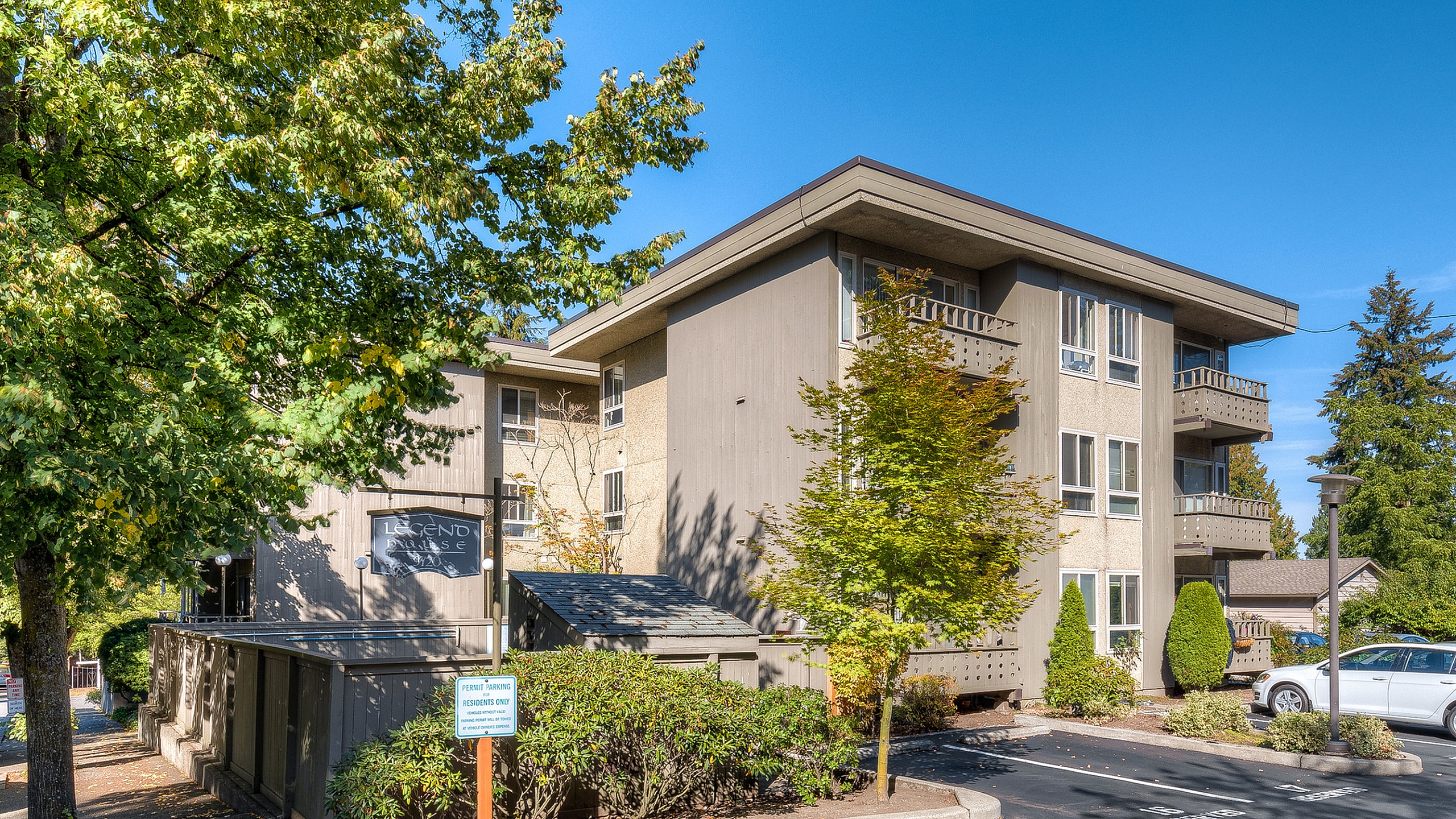 Charming apartment building surrounded by lush greenery and ample parking under a bright blue sky.