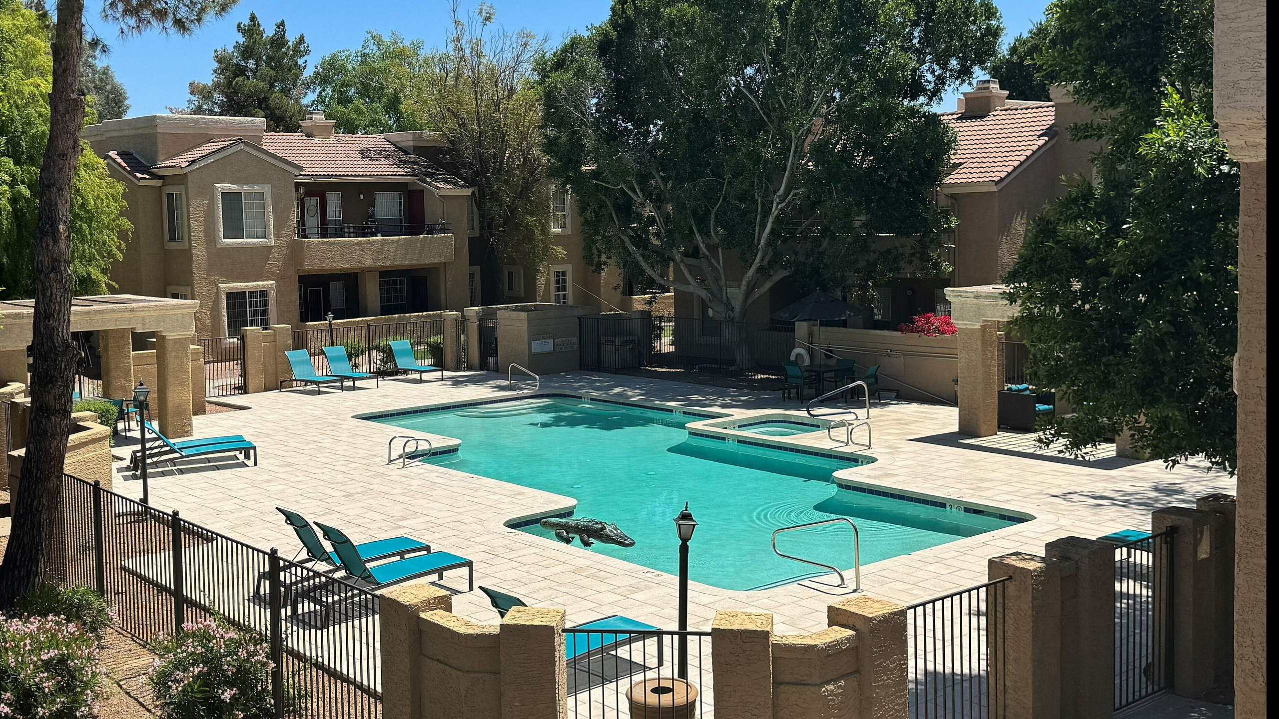 Inviting apartment complex with a sparkling pool, surrounded by lush greenery and modern lounge chairs, offering a serene escape.