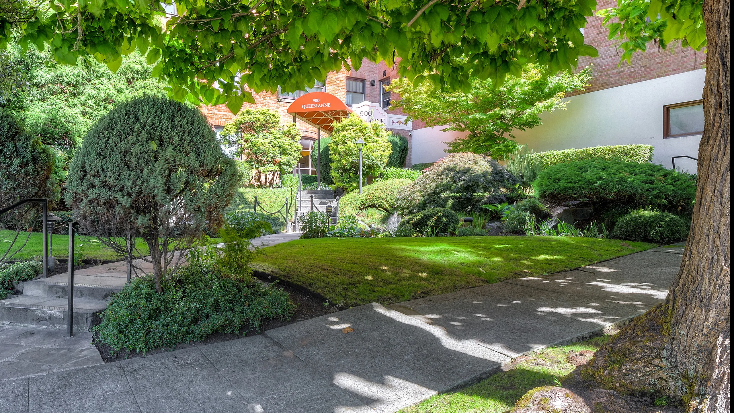 Charming entrance to Queen Anne apartments, surrounded by lush greenery and manicured landscaping.
