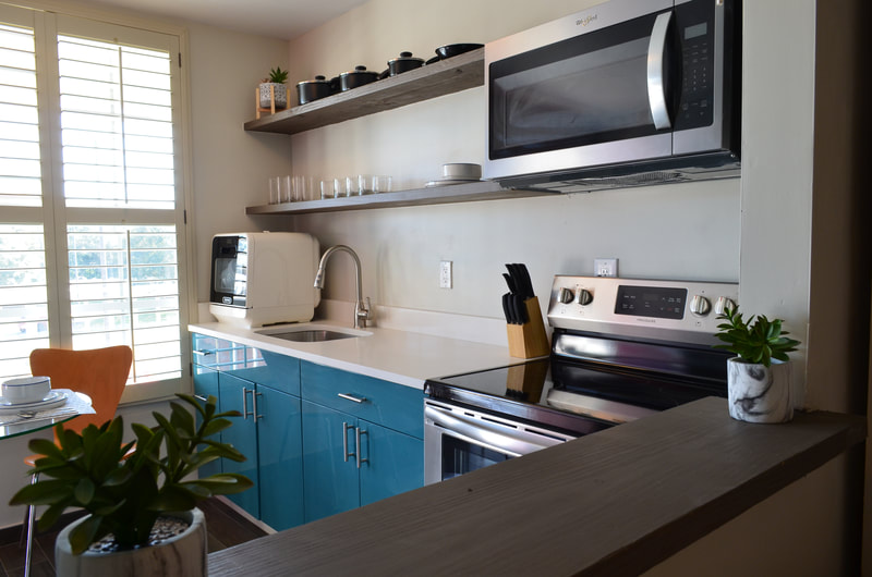 Chic modern kitchen with vibrant blue cabinets, sleek countertops, and stainless steel appliances, enhanced by natural light from large windows.