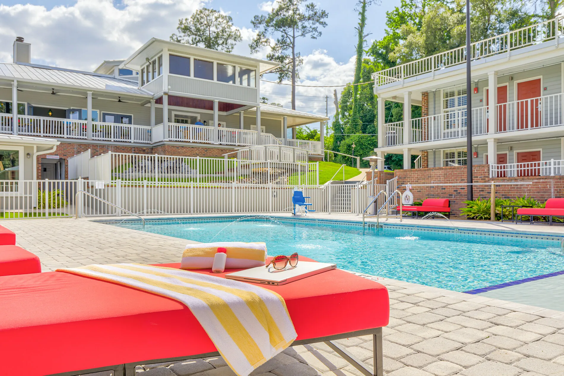 Modern apartment complex with a sparkling pool, vibrant red loungers, and spacious outdoor seating, perfect for relaxation.