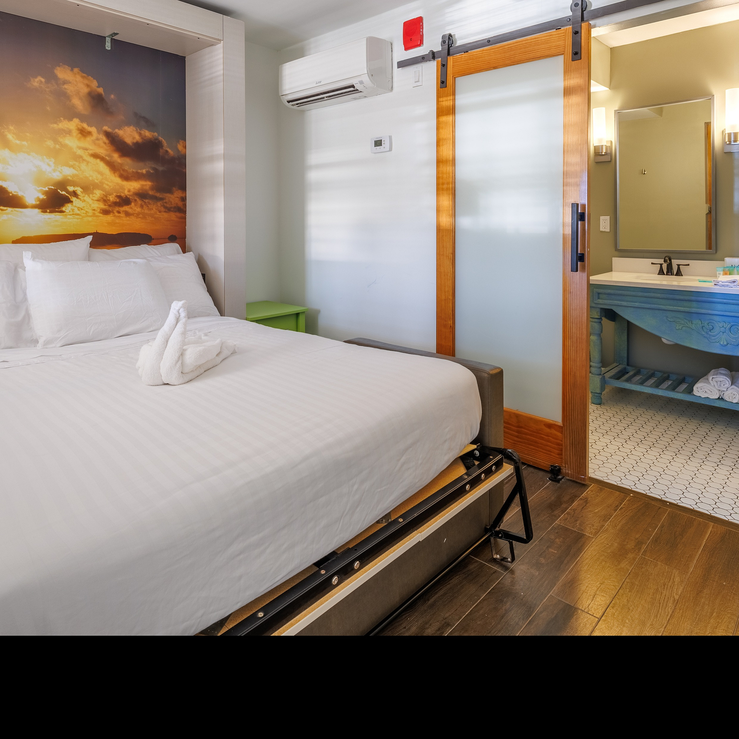 Bright and cozy bedroom with a sunset wall mural, modern ceiling fan, and sliding barn door leading to a stylish bathroom.