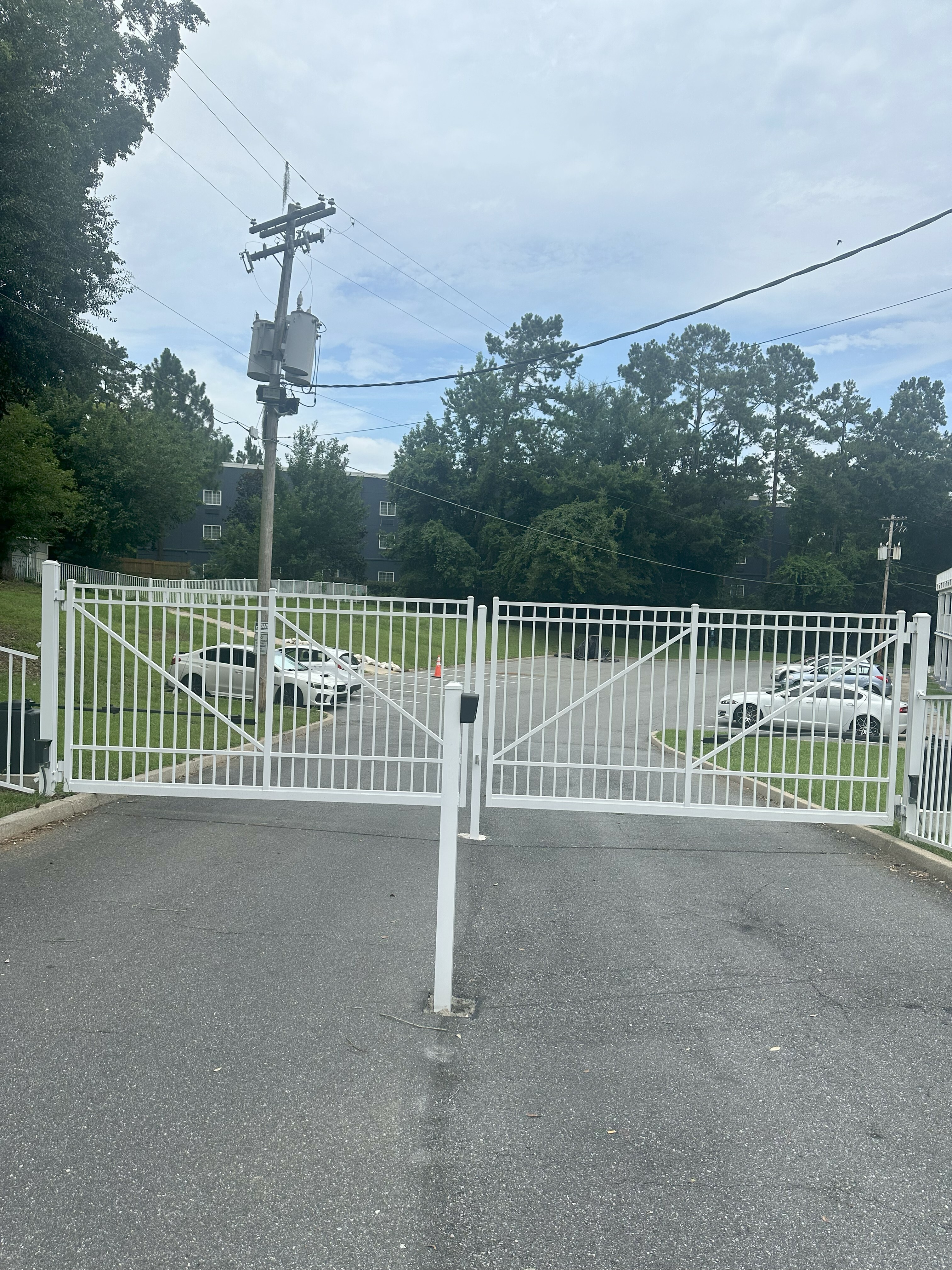 Secure entrance with white gates leading to a serene residential area, surrounded by lush greenery and a modern fountain of privacy.