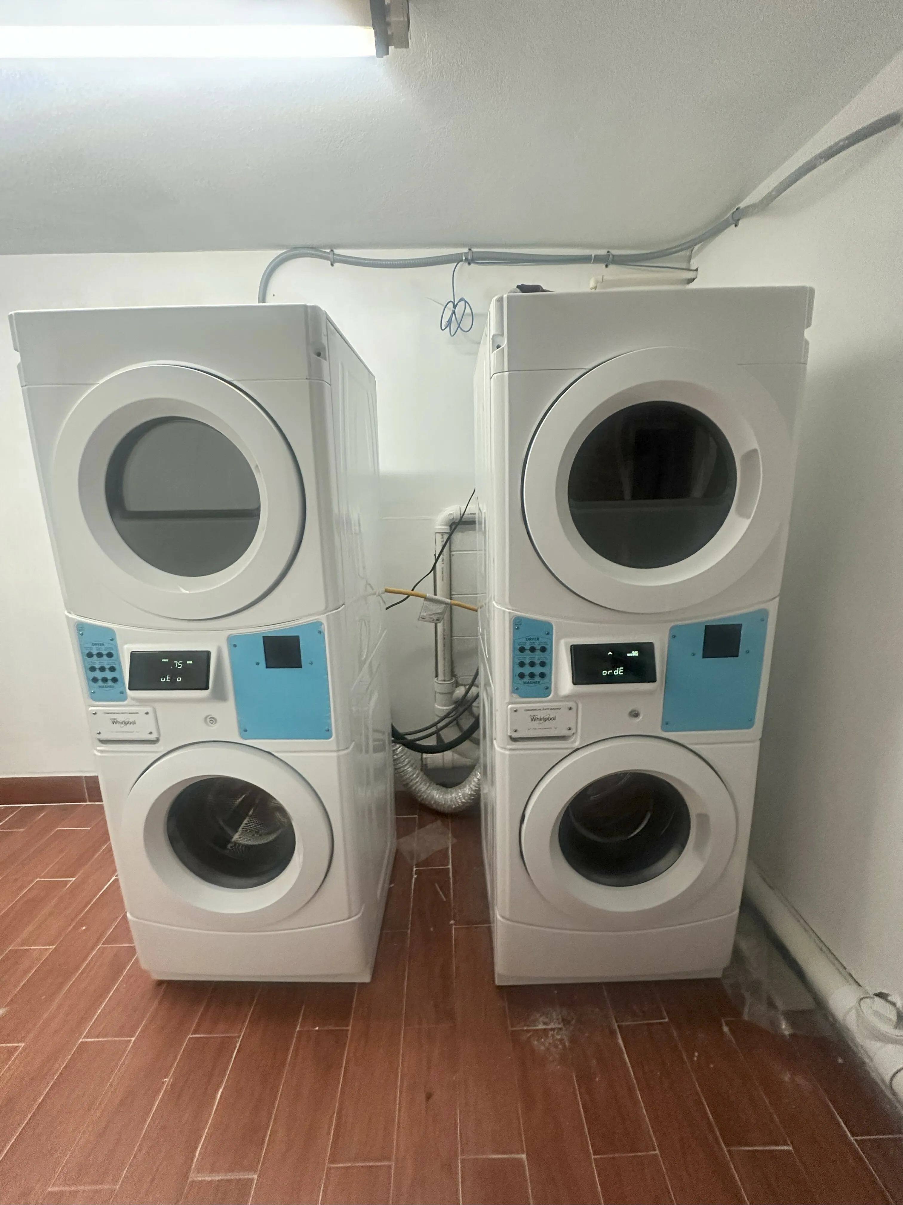 Modern laundry room featuring two sleek, stacked washing and drying machines with vibrant blue accents, set against warm wooden flooring.