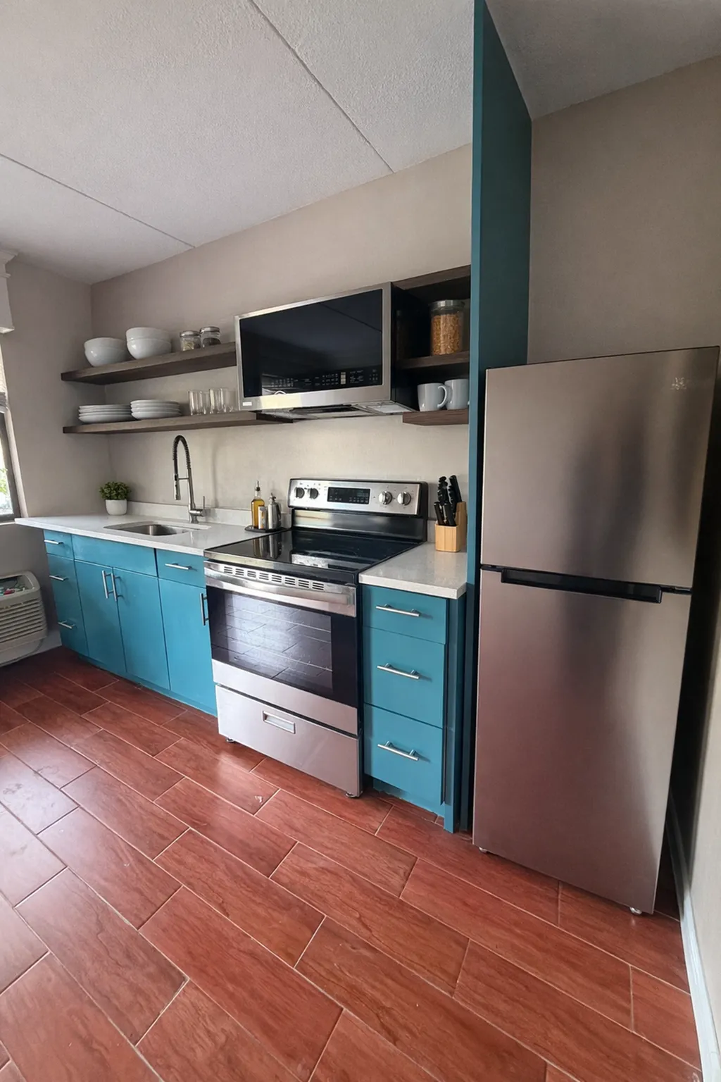 Modern kitchen with vibrant teal cabinets, stainless steel appliances, and open shelving for a chic, functional space.