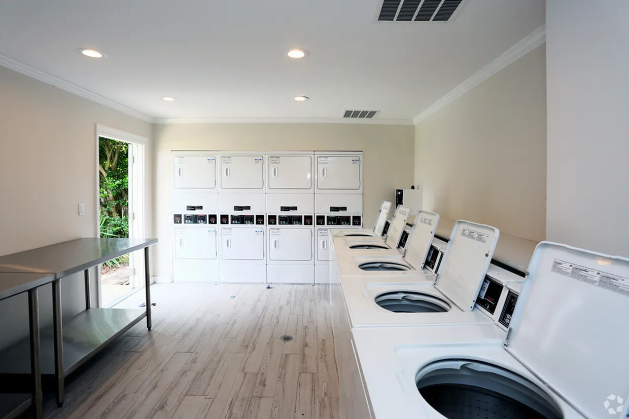 Bright and modern laundry room featuring multiple washing machines and dryers, complemented by stylish flooring and ample natural light.