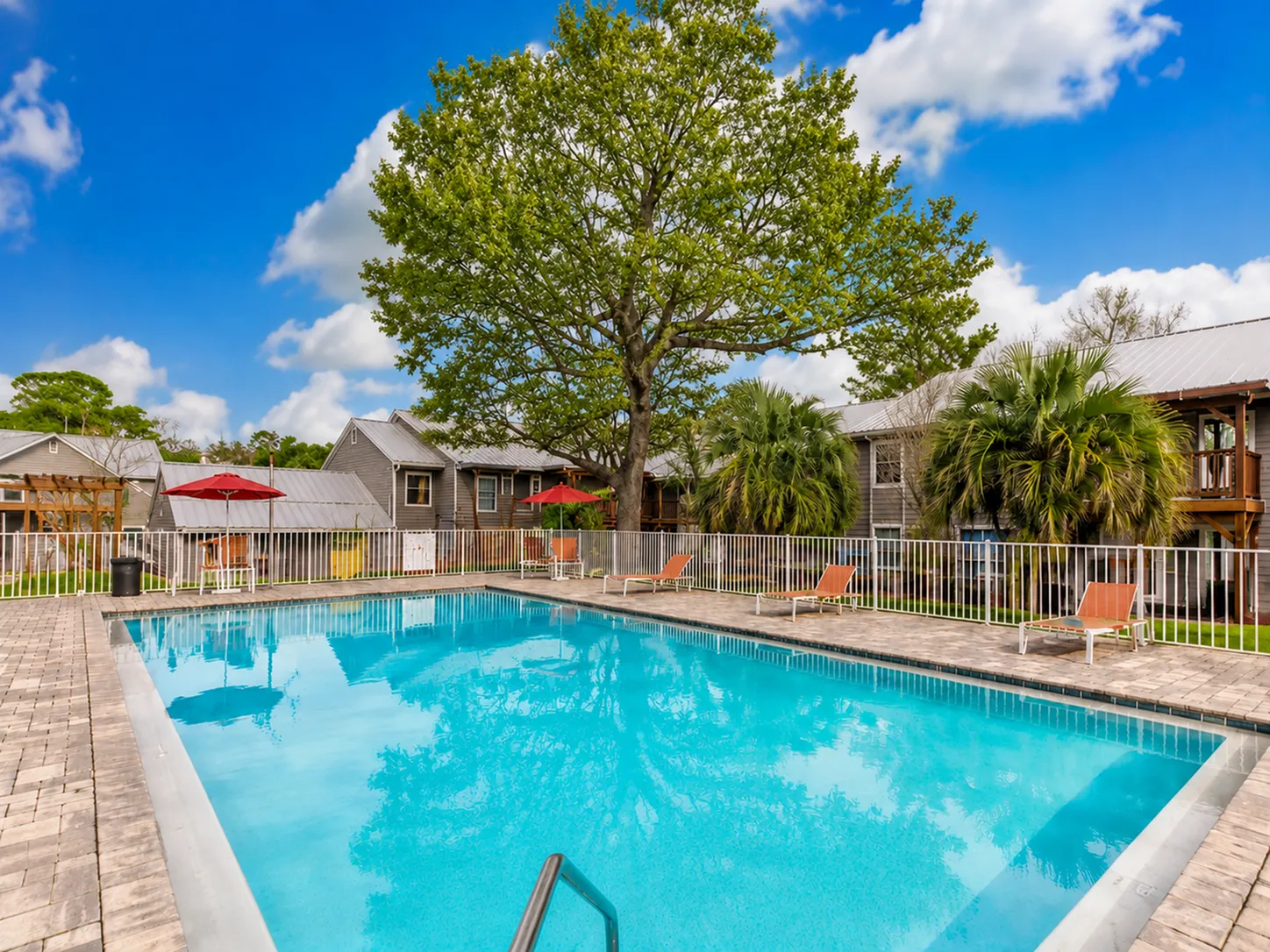 Charming apartment complex with inviting pool area, surrounded by lush greenery and cozy outdoor seating.