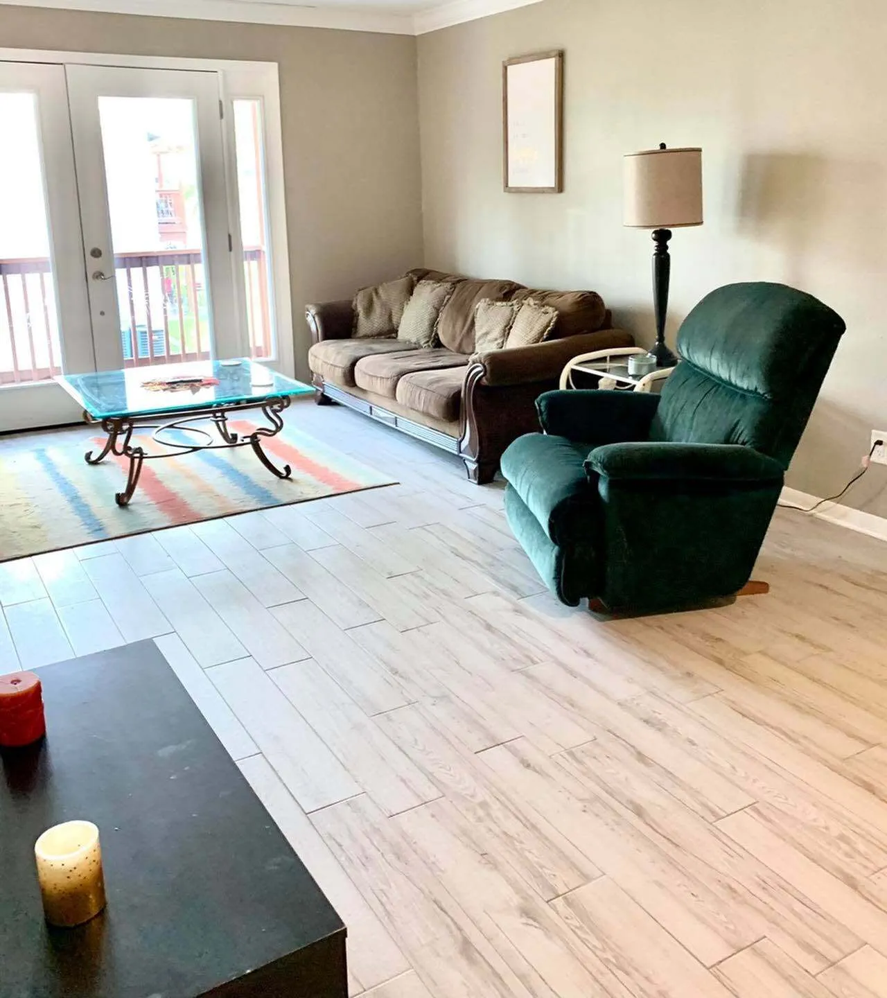 Bright and inviting living room with a cozy brown sofa, elegant coffee table, and plush recliner set against a backdrop of light wood flooring and large windows.