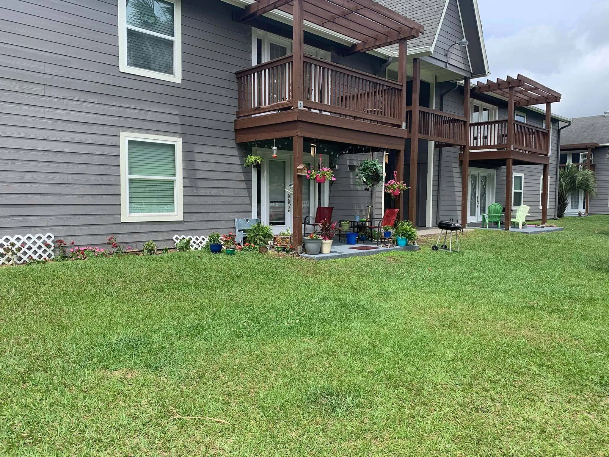 Charming suburban apartment exterior featuring private balconies, lush green lawn, and vibrant floral decorations.