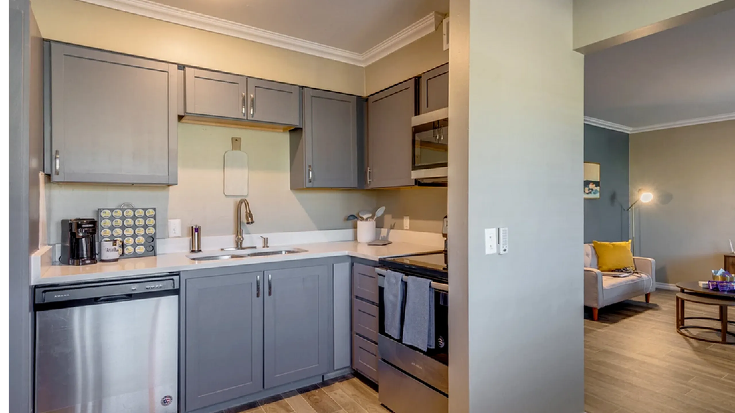 Modern kitchen with sleek grey cabinetry, stainless steel appliances, and open-concept living area adorned with stylish decor.