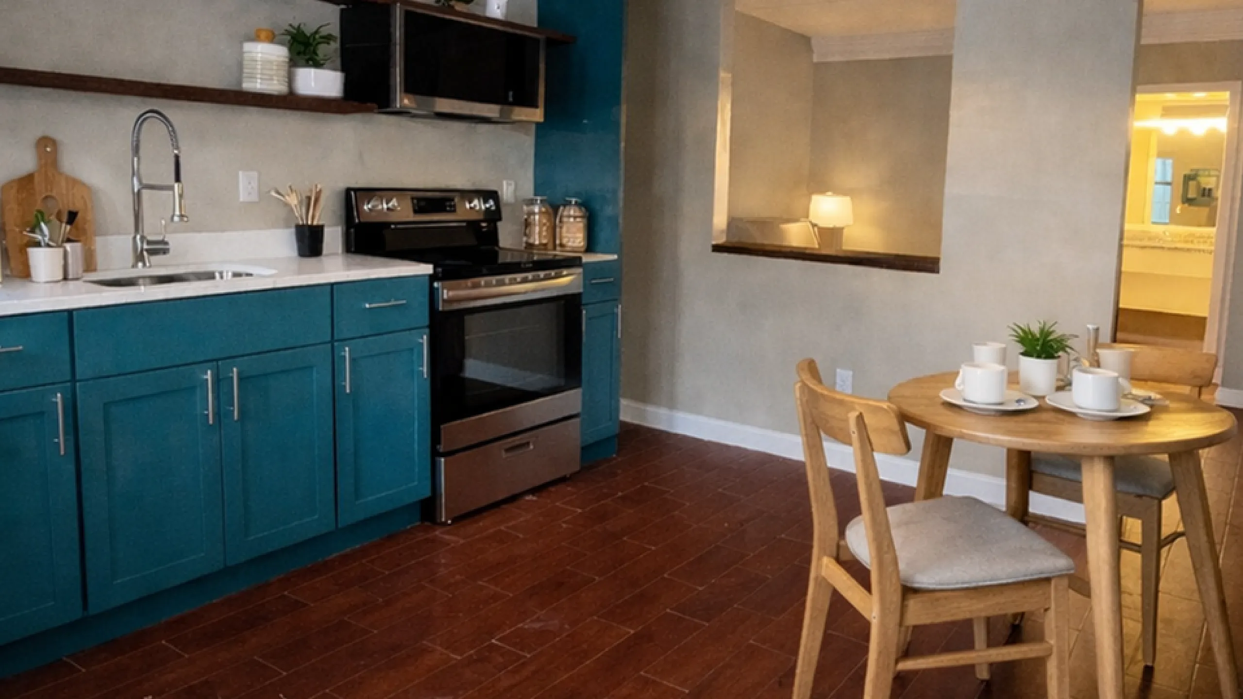 Inviting kitchen with elegant teal cabinetry, modern appliances, and cozy dining area on rich wooden floors.
