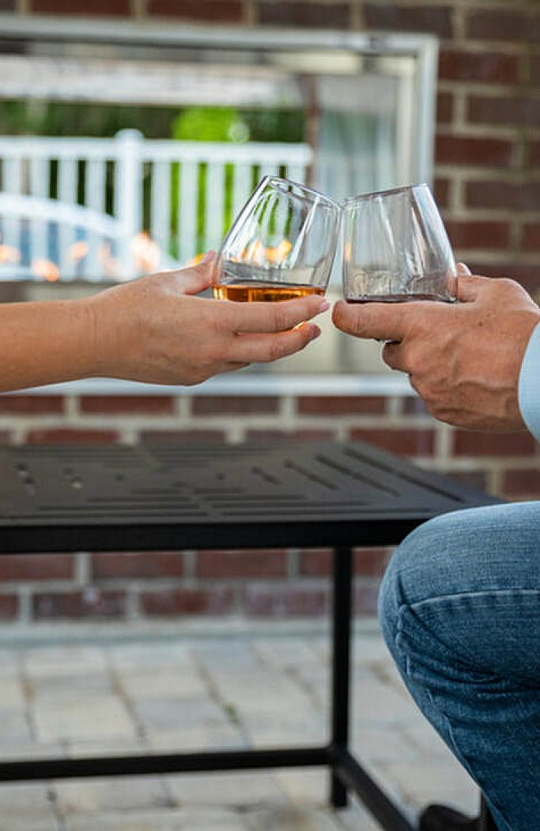 Inviting patio scene with two people toasting drinks by a cozy outdoor fire, surrounded by elegant brickwork.