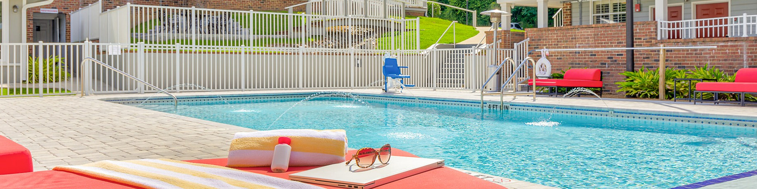 Inviting modern pool area with bright red loungers, perfect for relaxation, surrounded by elegant apartment buildings and lush greenery.