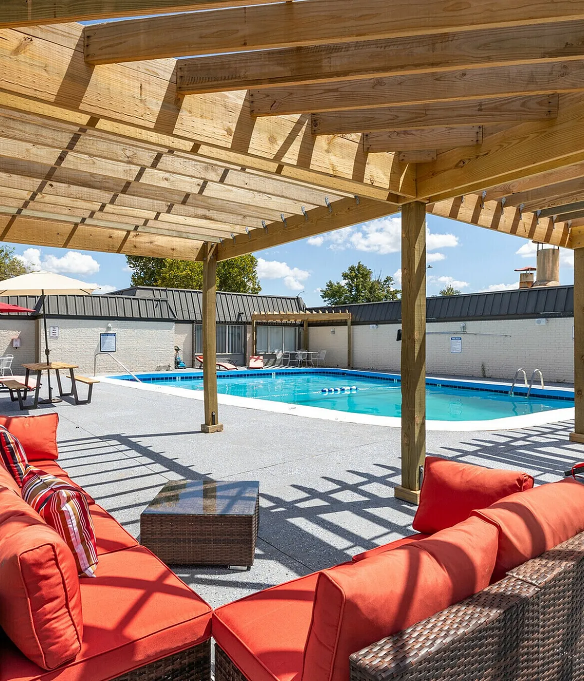 Inviting outdoor pool area with cozy red-cushioned seating under a wooden pergola, perfect for relaxation and soaking up the sun.