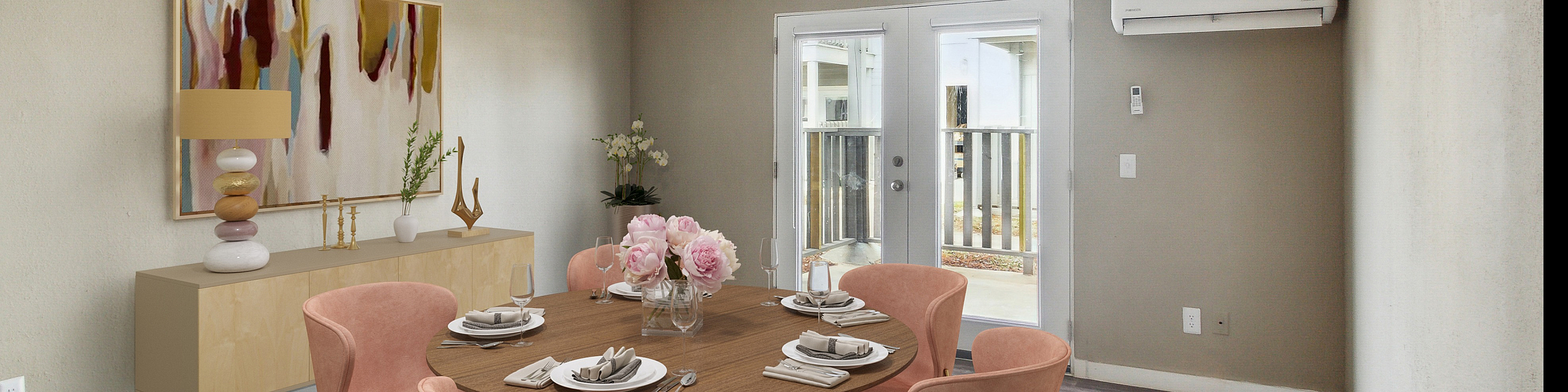 Elegant dining room with modern decor, featuring a round wooden table, plush pink chairs, and contemporary art. Bright, airy space with natural light from glass doors and a sleek ceiling fan.