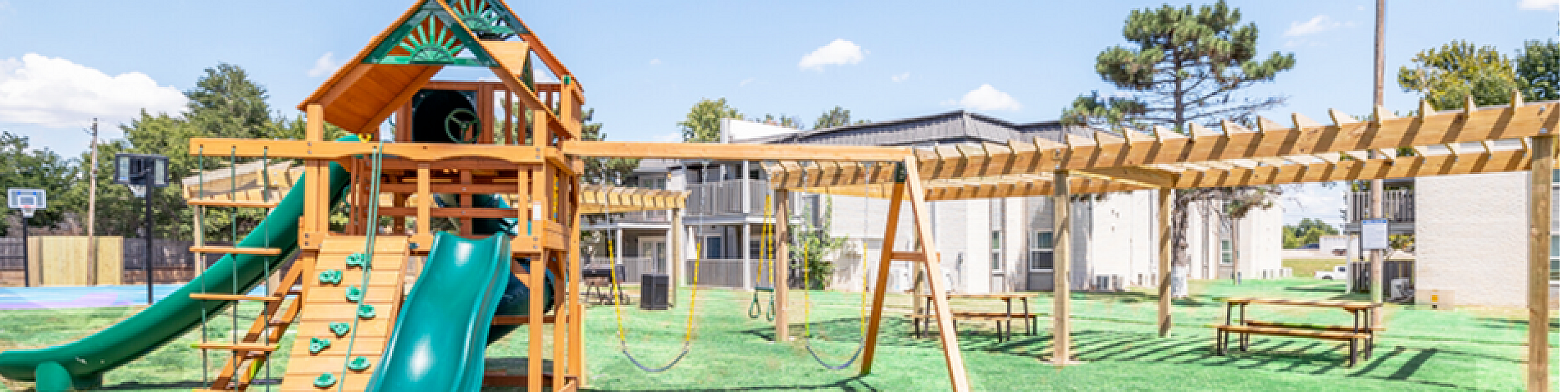 Vibrant playground with wooden climbing frame and slides in a lush green apartment complex, perfect for family fun.
