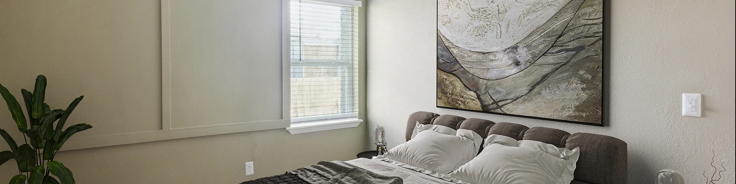 Inviting and serene bedroom featuring a plush bed, elegant artwork, and natural light streaming through large windows.
