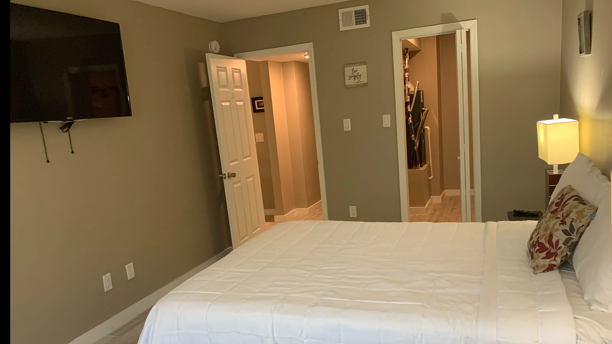 Inviting bedroom showcasing a plush bed with stylish pillows, ambient lighting, and a wall-mounted TV in a modern apartment.