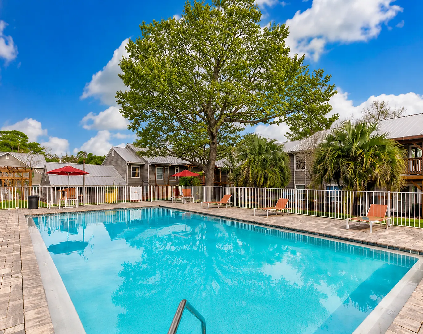 Inviting community pool surrounded by lush greenery and cozy patio seating, offering serene and relaxing atmosphere.