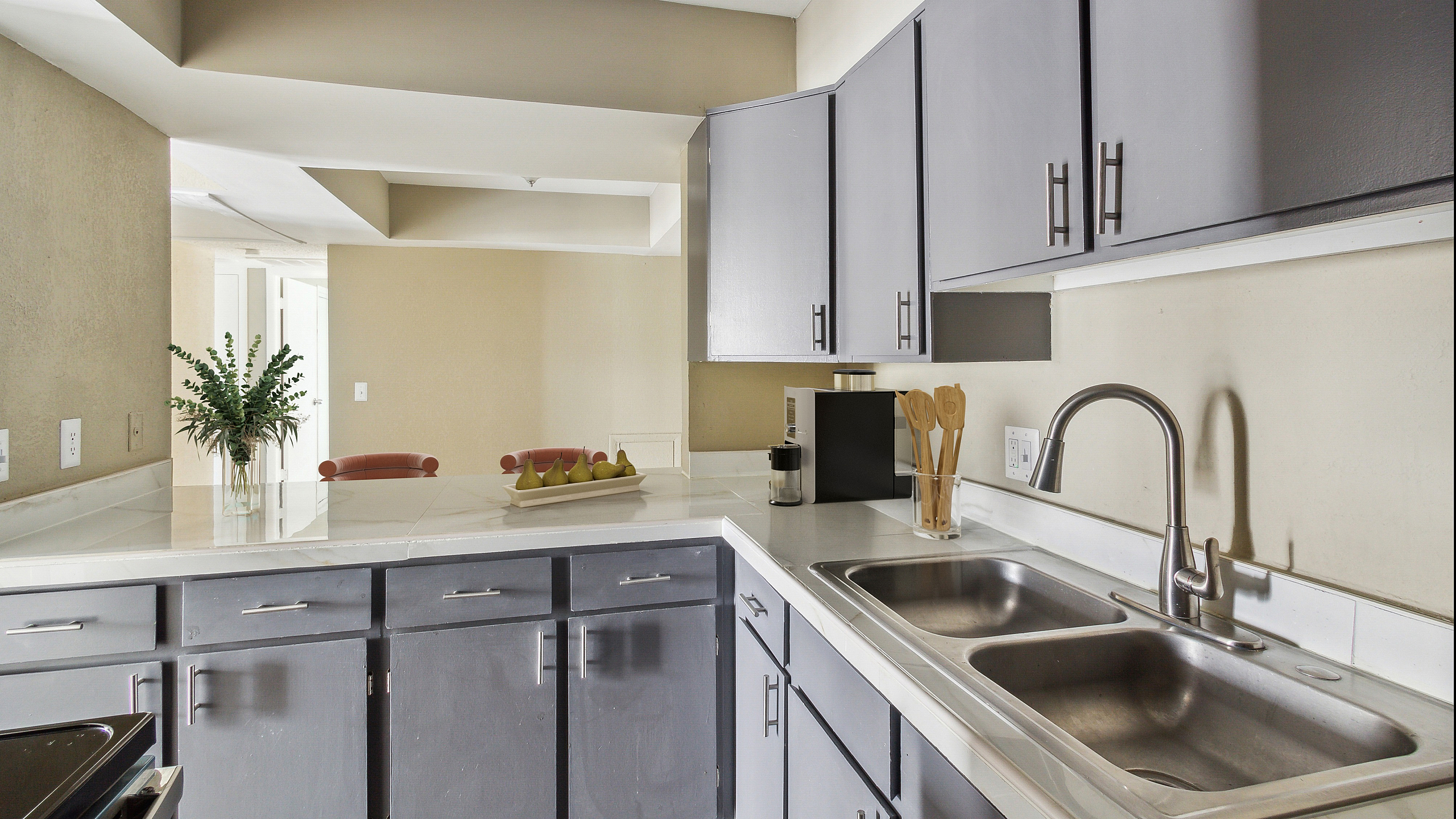 Modern kitchen design with sleek gray cabinets, dual sink, and chic decor featuring a fruit arrangement and greenery.