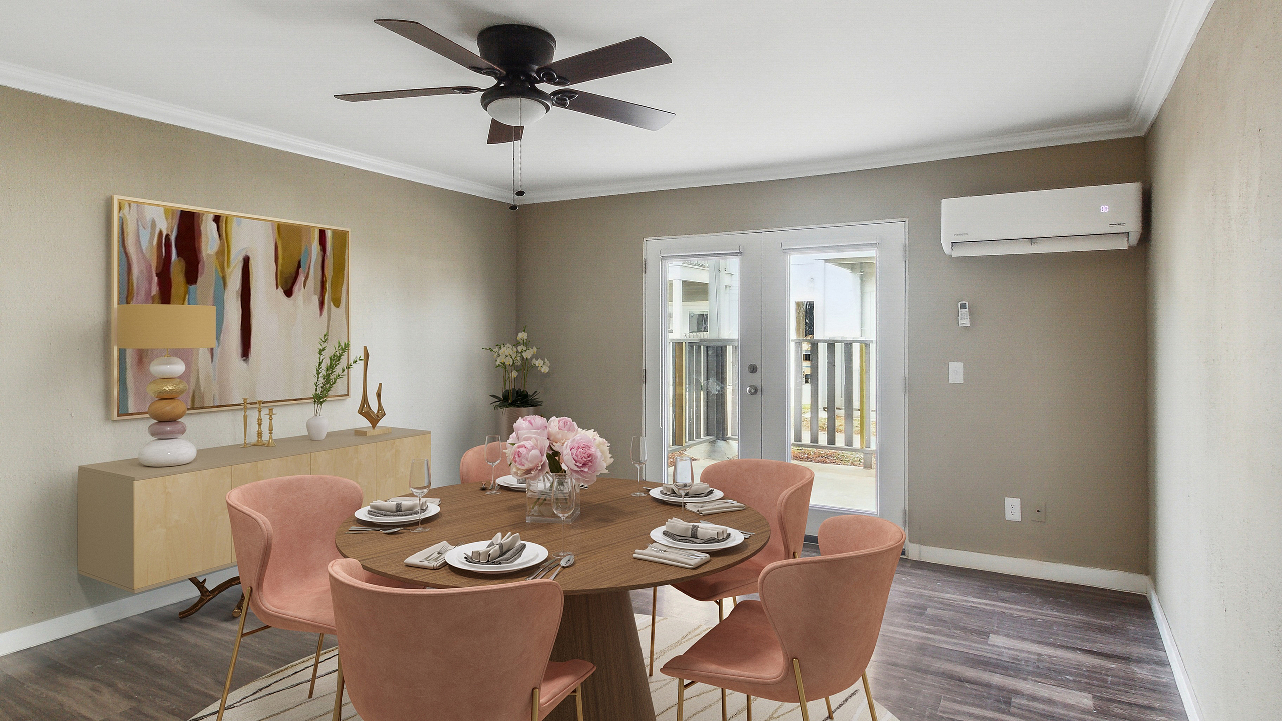 Elegant dining room featuring a round wooden table with plush pink chairs, artistic decor, and abundant natural light through French doors.