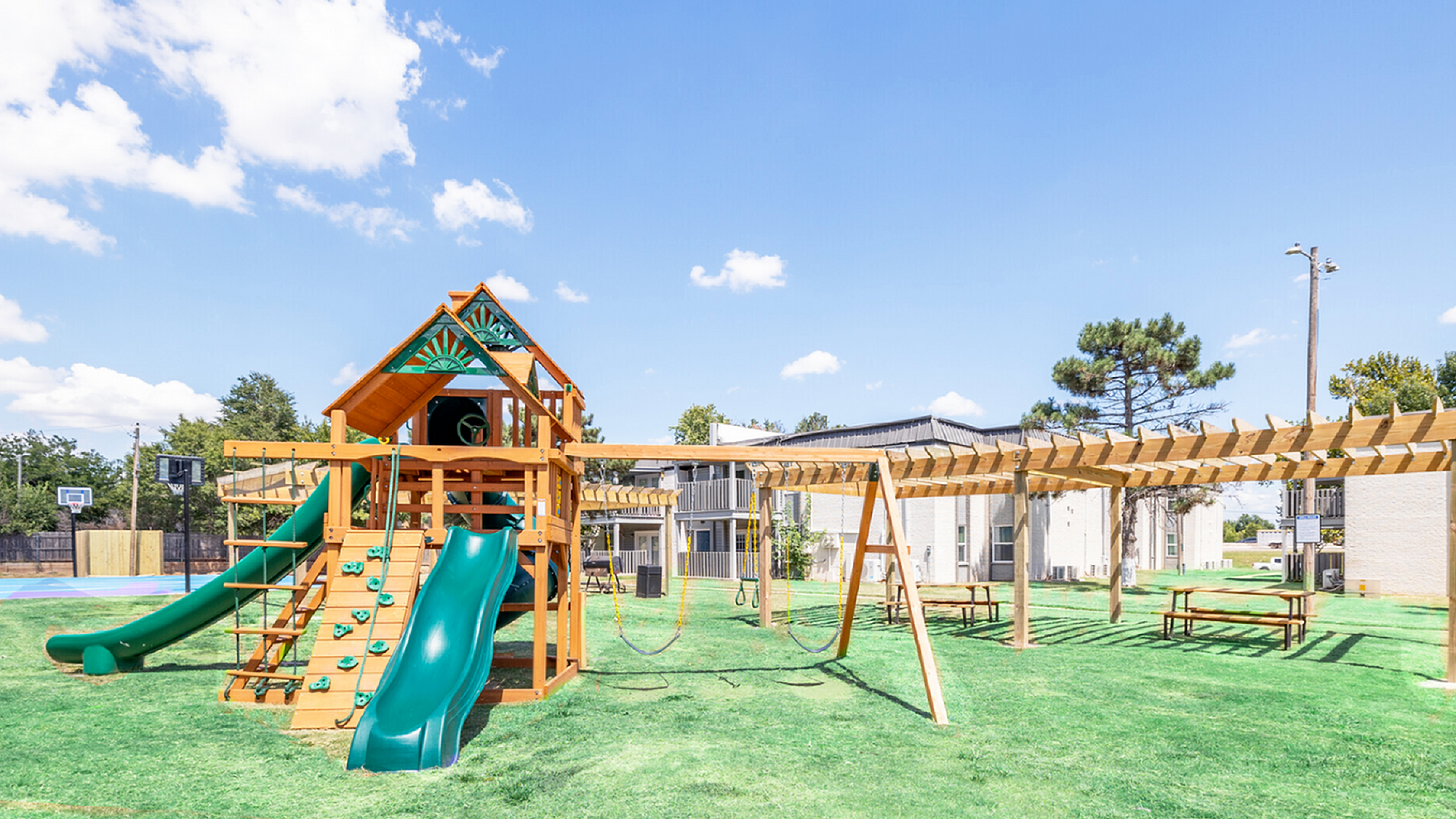 Vibrant community playground with a wooden playset, swings, and picnic area surrounded by lush greenery, perfect for family fun.