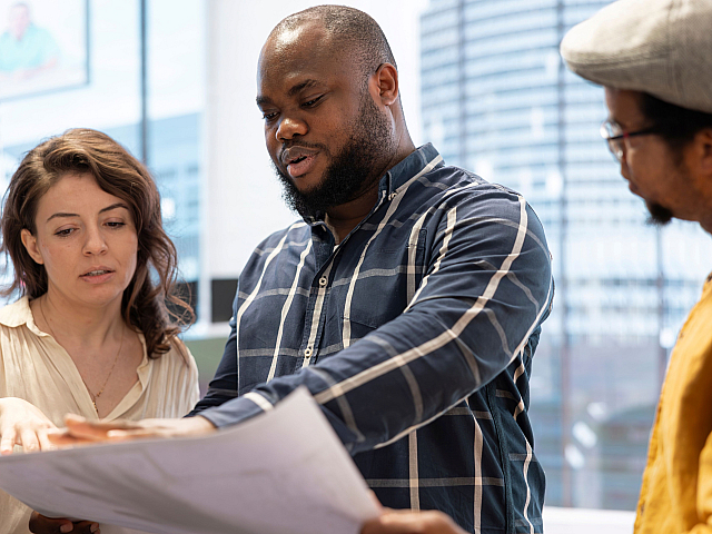 Three professionals engaged in reviewing architectural plans in a modern, brightly lit office.