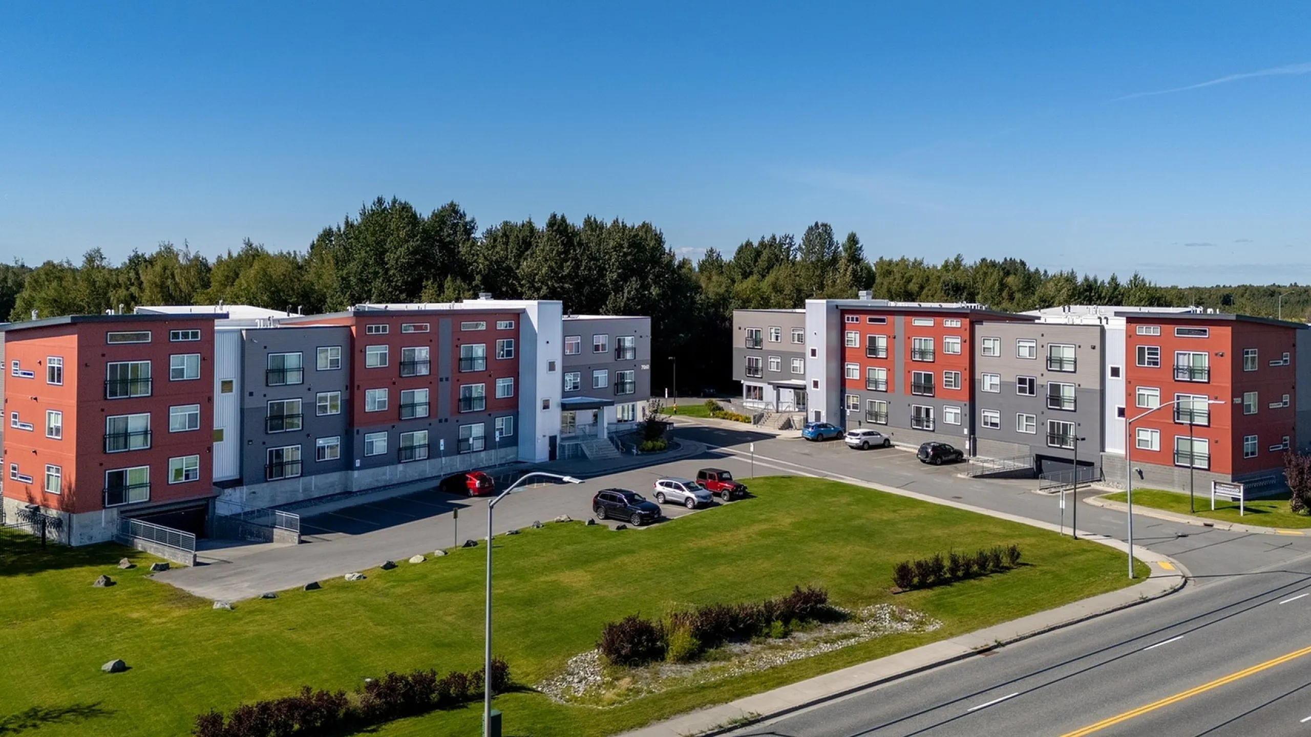 Modern apartment complex with vibrant facades, spacious lawns, and convenient parking, set against a serene wooded backdrop.