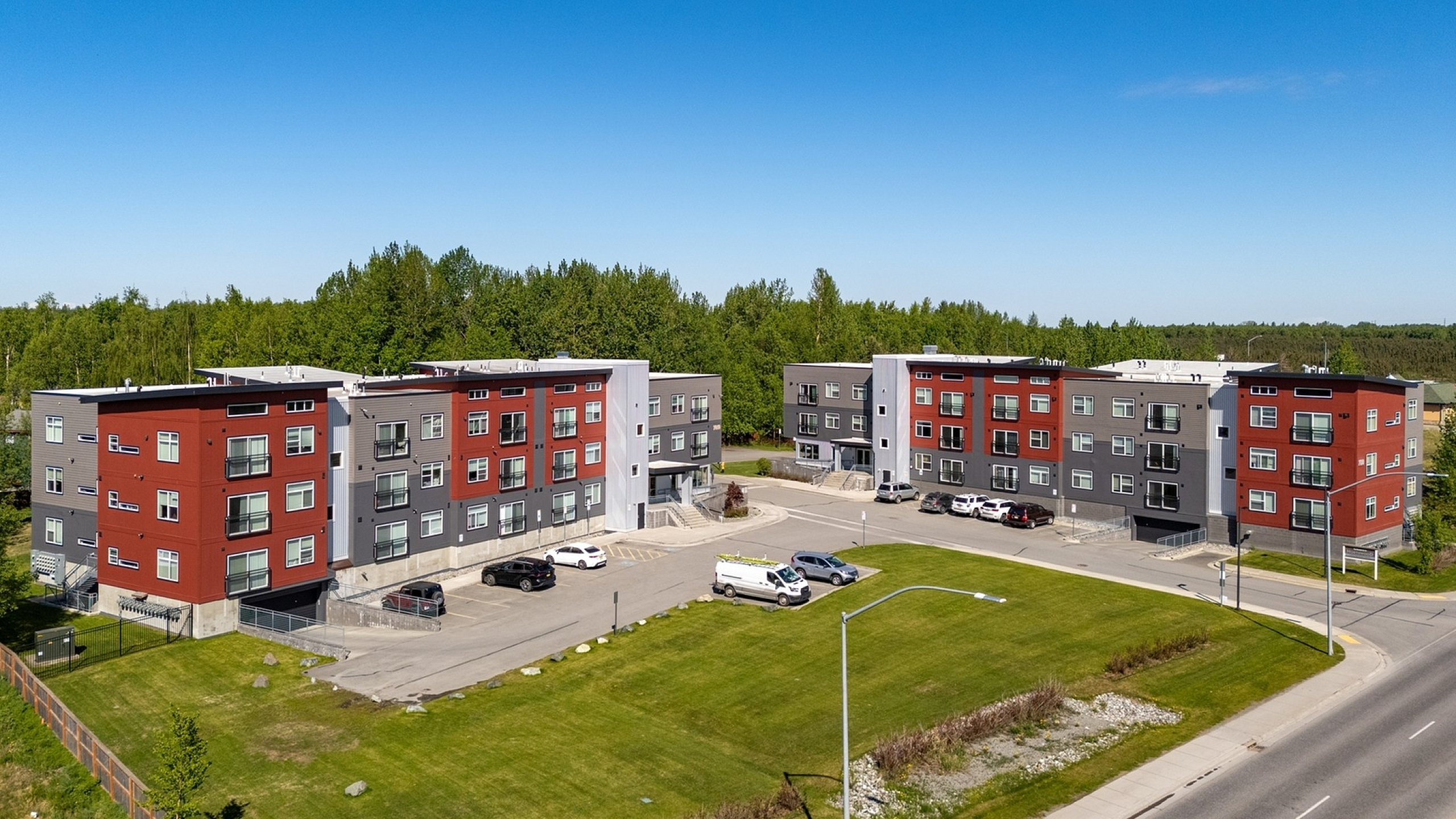 Modern apartment complex with vibrant red and gray exterior, surrounded by lush greenery and spacious parking, offering a desirable urban living experience.