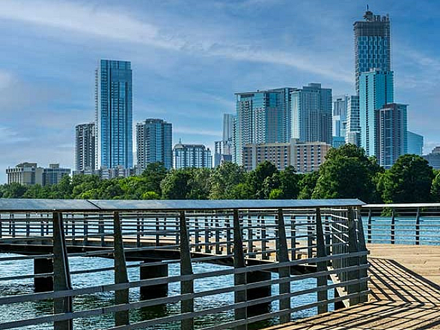 Vibrant cityscape featuring modern skyscrapers overlooking a serene waterfront with a picturesque boardwalk.