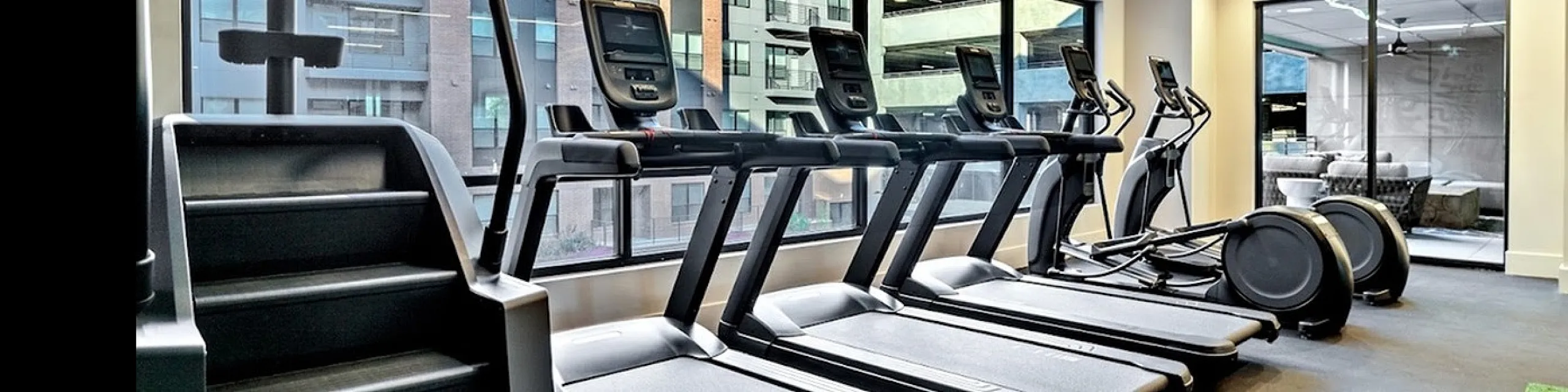 Sleek fitness room featuring modern treadmills and exercise bikes with large windows offering city views.